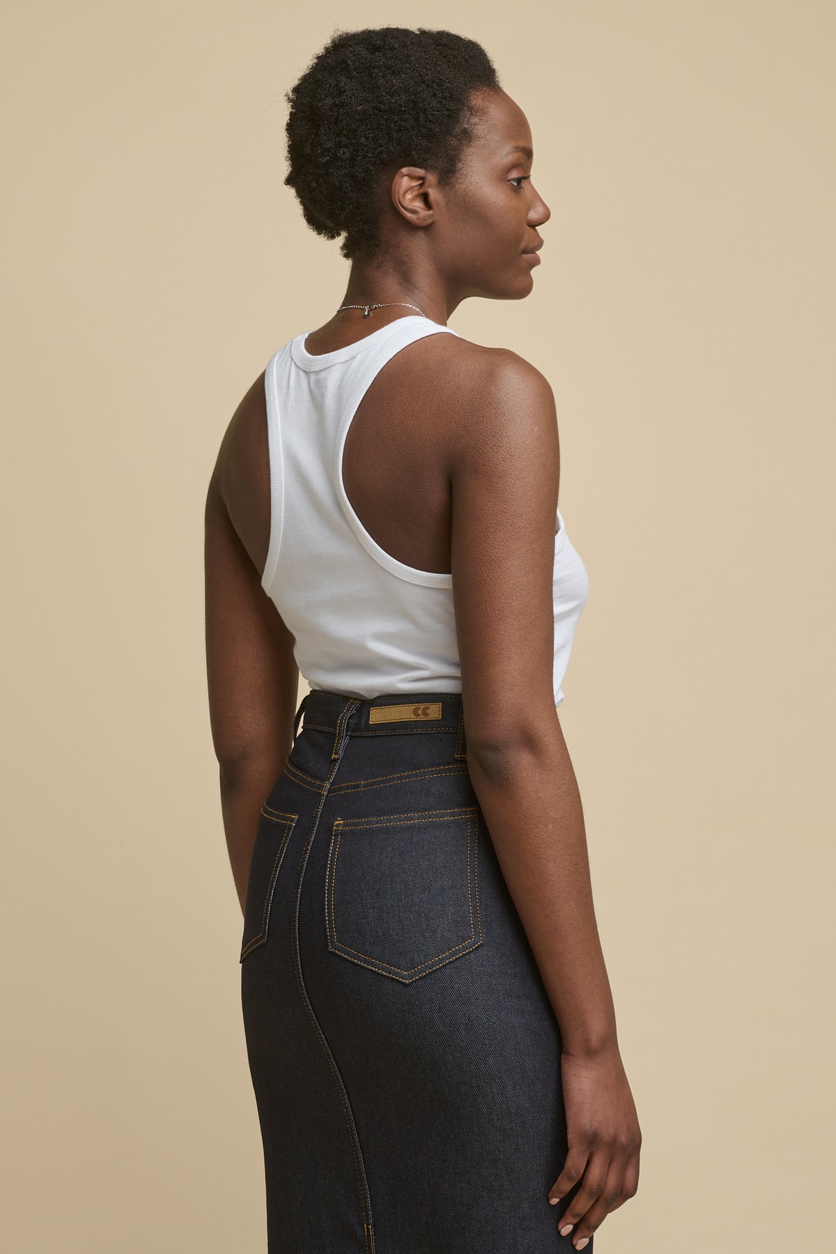 Thigh up image of the back of female wearing Frankie denim maxi skirt in indigo with small rectangular CC logo jeans patch on the waist band and two back pockets