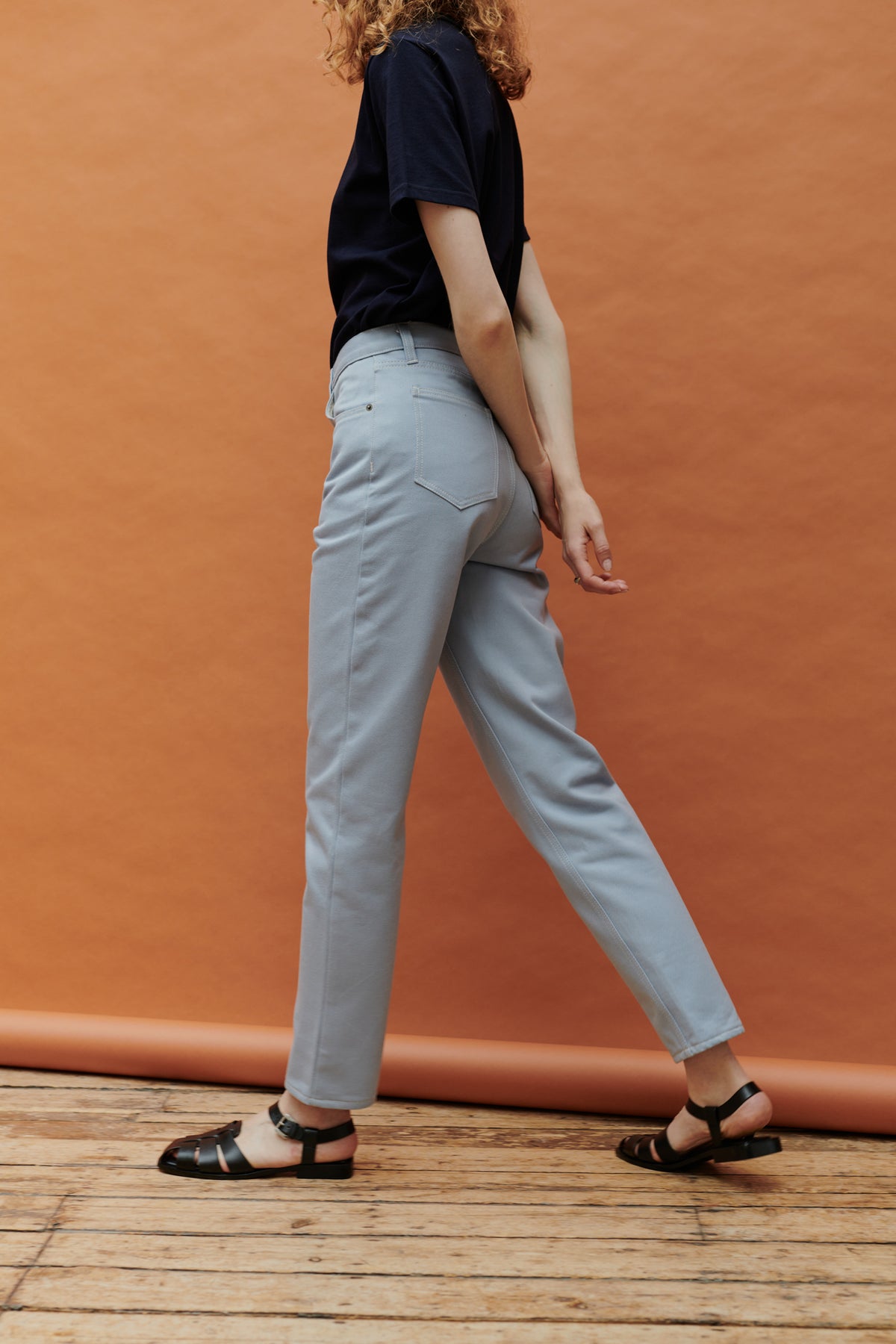 White female with curly ginger shoulder length hair wearing Community Clothing Gloria tapered jeans in light blue paired with navy short sleeve t shirt tucked in