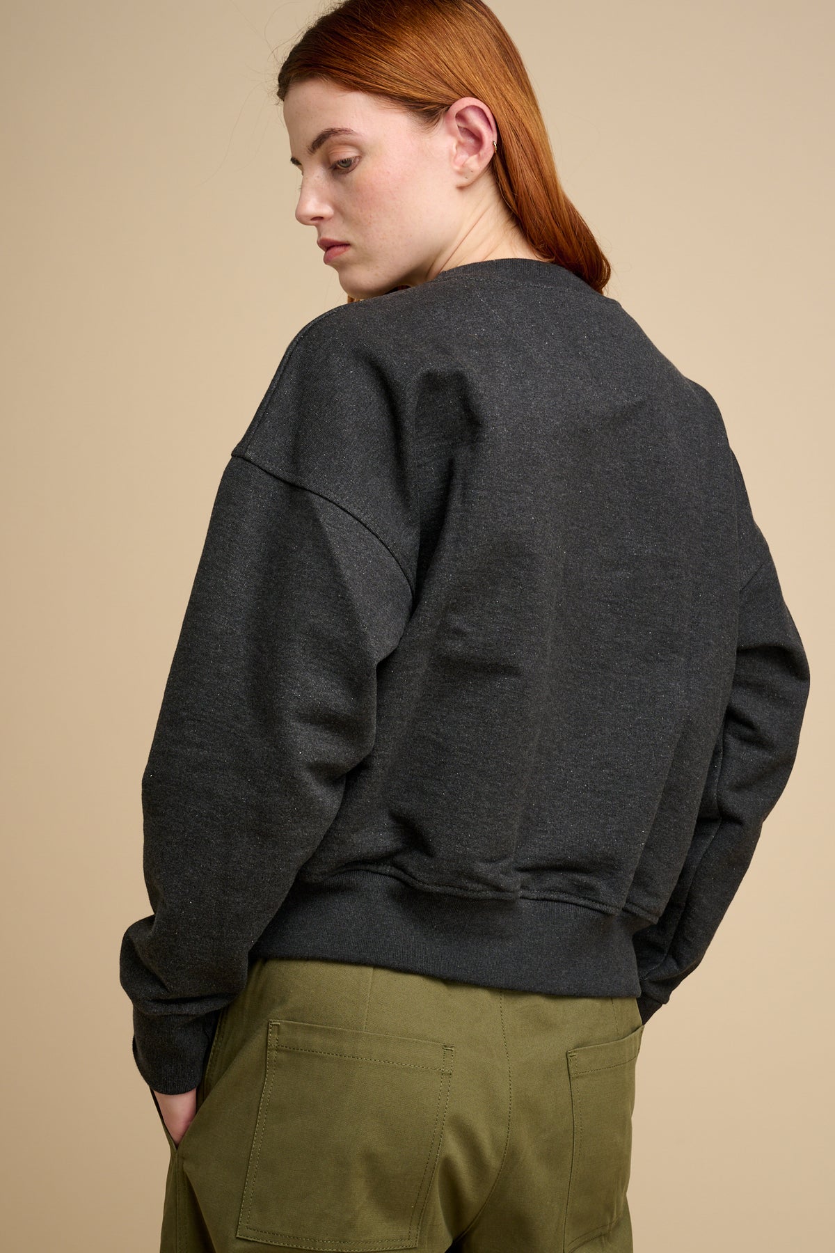The back of woman wearing charcoal heavyweight sweatshirt with olive trousers.