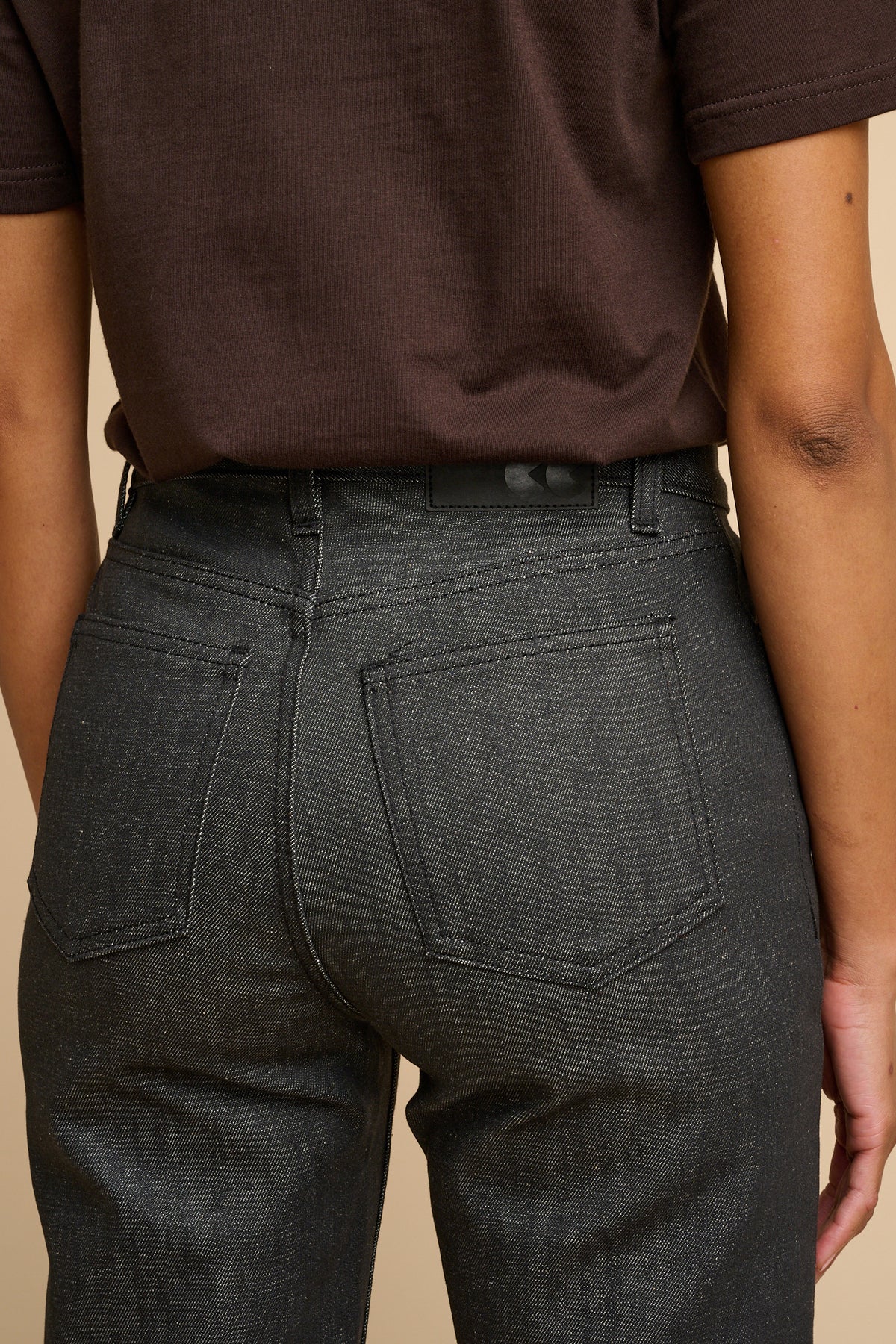 Woman wearing black jeans and a brown T-shirt against a beige background