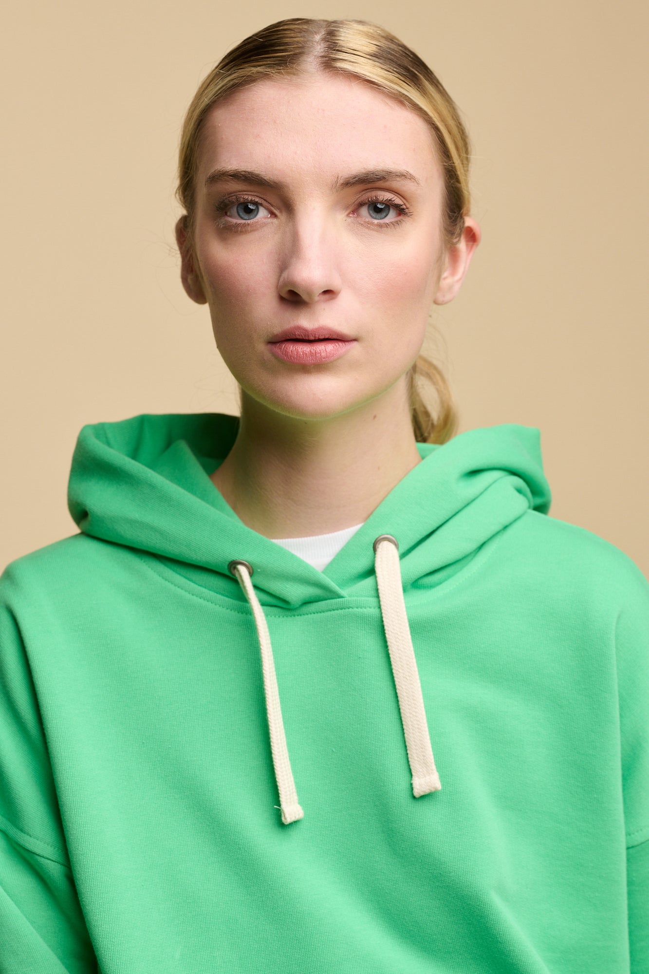 Thigh up image of female wearing hooded sweatshirt in apple green worn over white crew neck t shirt with blue jeans.