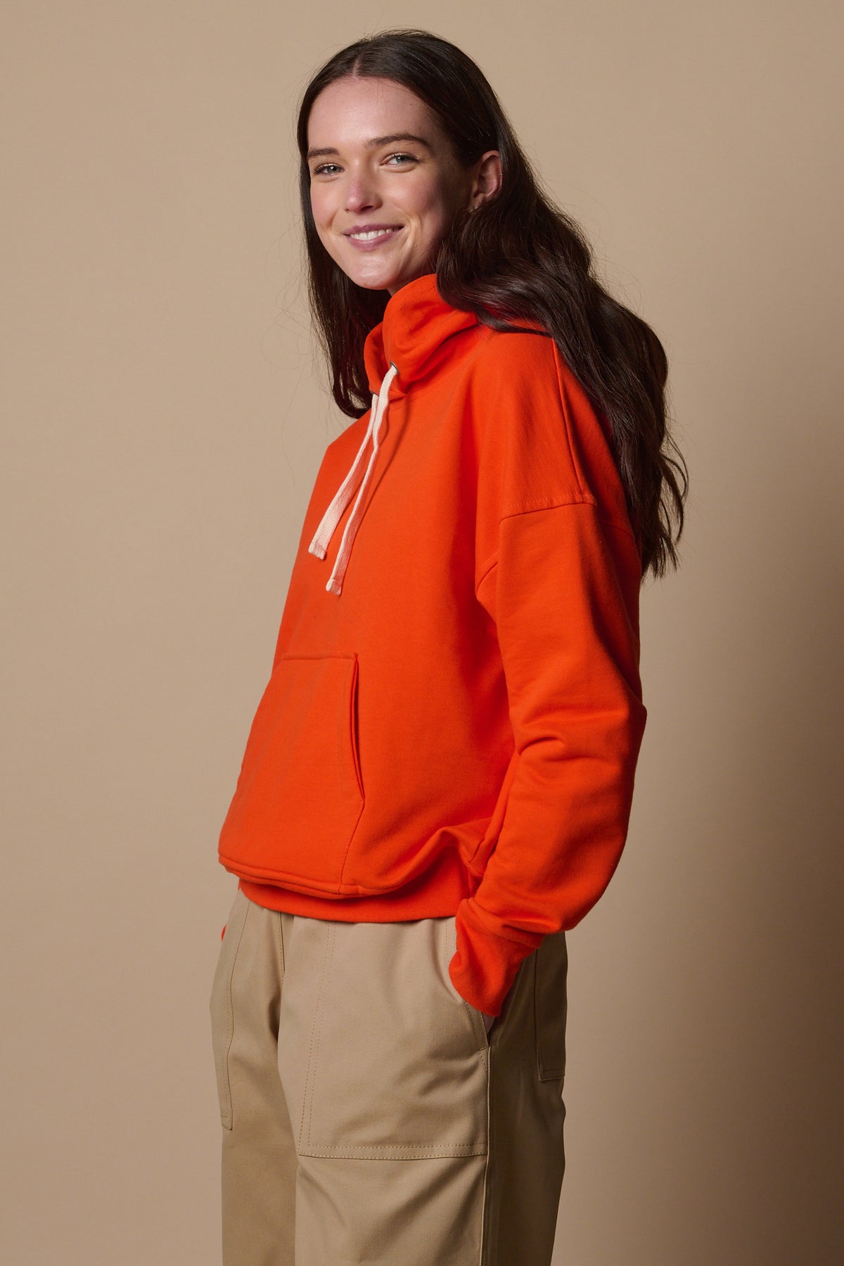 Thigh up image of the side of smiley female wearing hooded sweatshirt in flame red. 