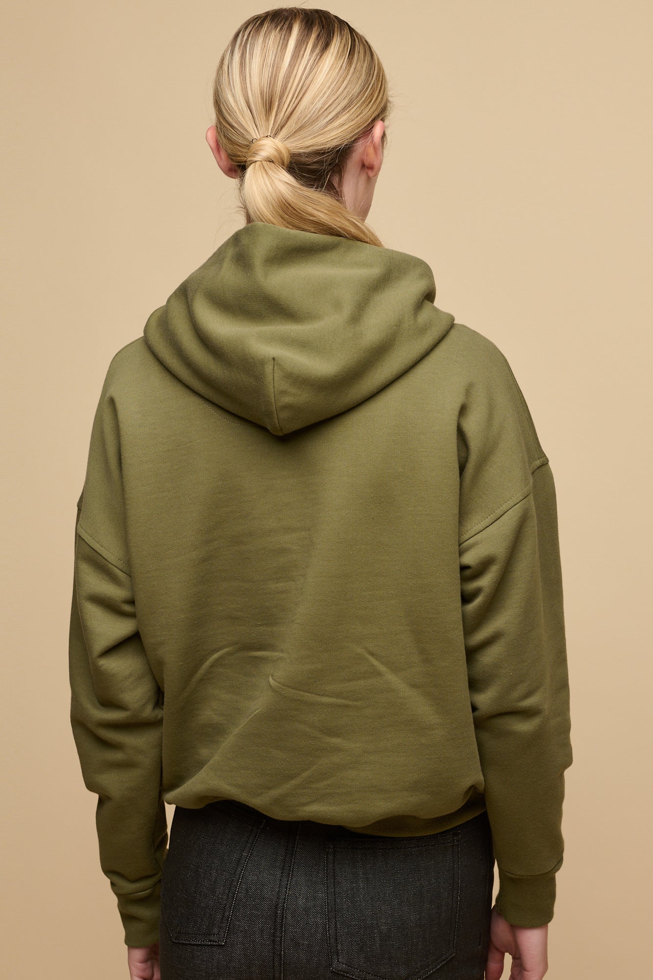 Thigh up image of blonde female wearing hooded sweatshirt in olive with one front pocket, worn over white crew neck t shirt paired with denim maxi skirt in black