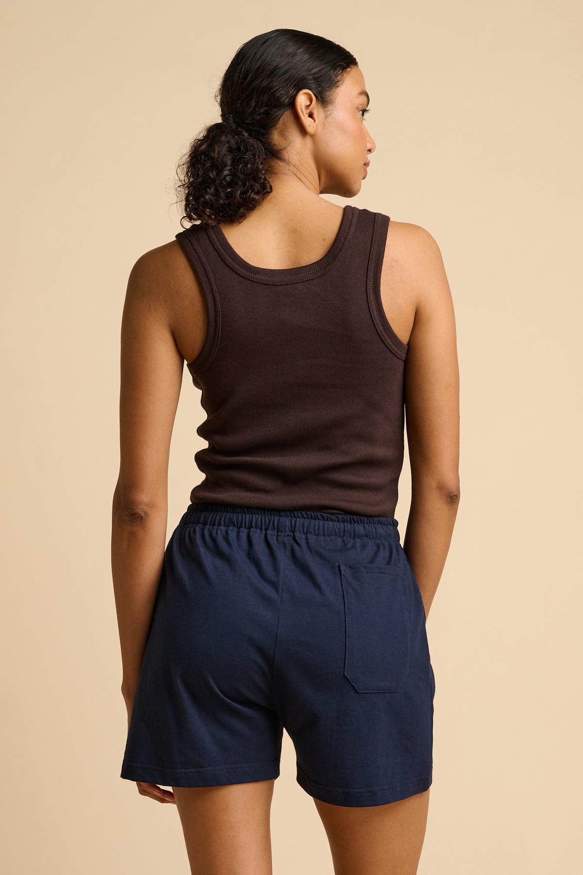 Woman wearing a brown tank top and navy shorts on a beige background