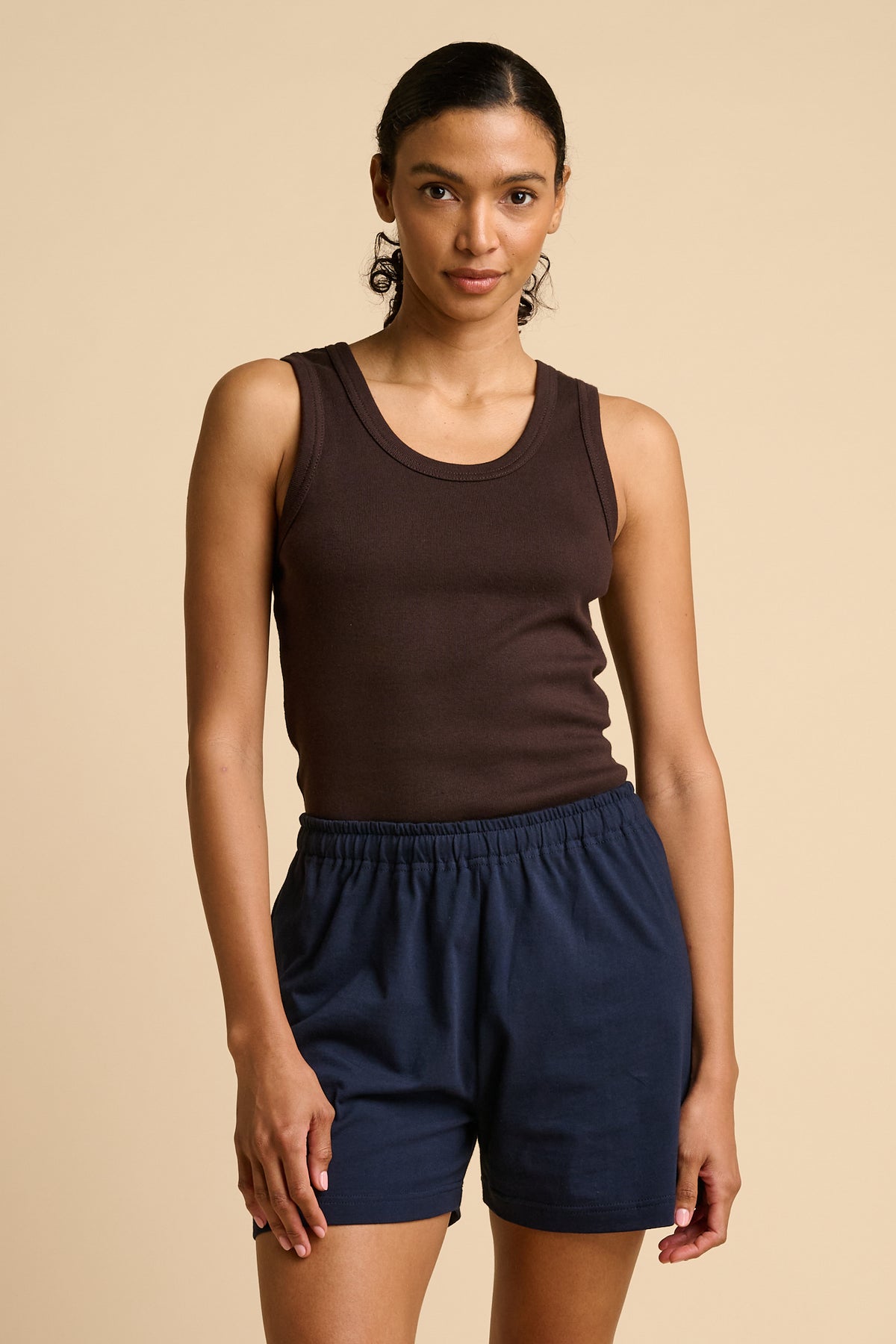 Woman wearing a brown tank top and navy shorts on a beige background