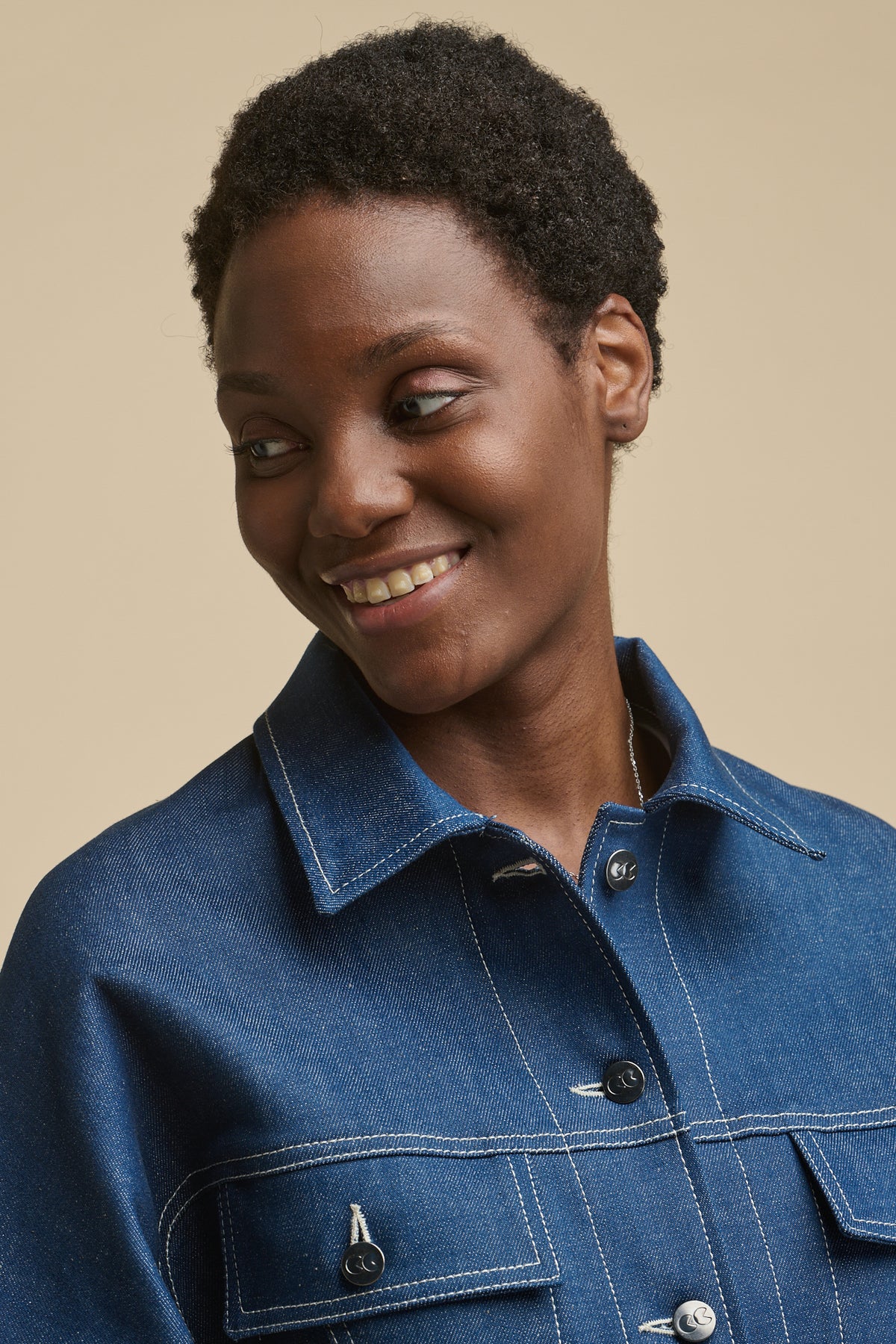 Portrait of smiley, black female wearing Jodie denim jacket in blue shwoing detail of CC logo buttons and two front chest pockets with flaps