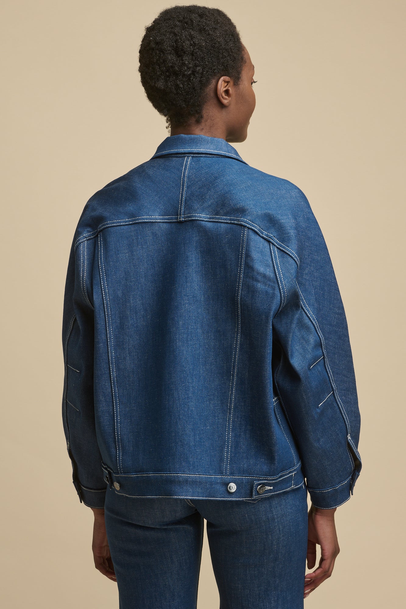 Portrait of smiley, black female wearing Jodie denim jacket in blue shwoing detail of CC logo buttons and two front chest pockets with flaps