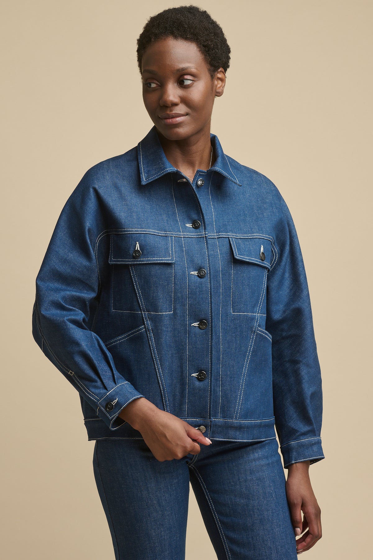 Thigh up image of the front of female wearing Jodie denim jacket in blue with two front pockets and two front chest pockets with flaps, button cuff and CC logo buttons