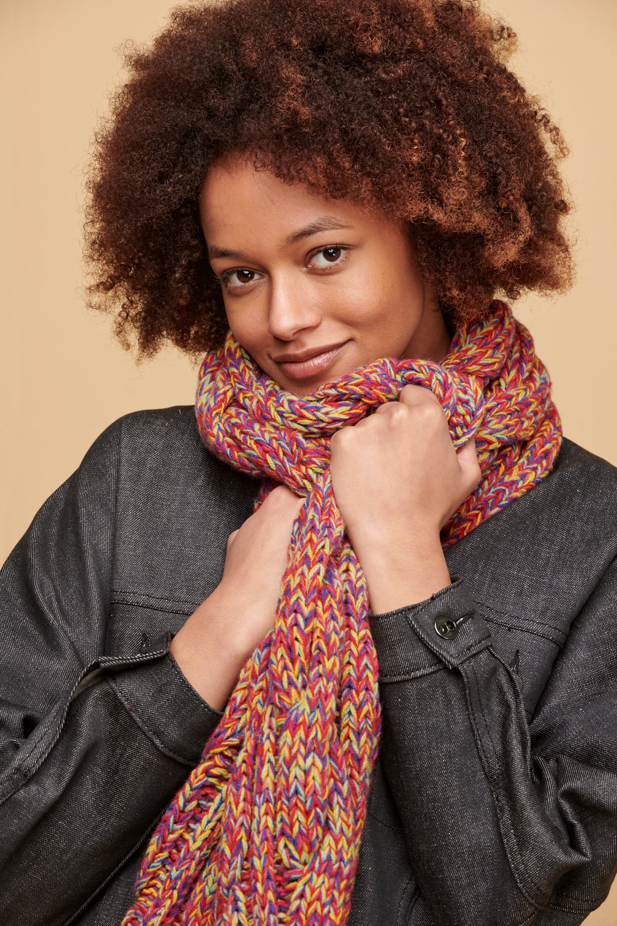 Female of colour with afro wearing unisex lambswool cable knit scarf in flame red marl with Jodie denim jacket in black
