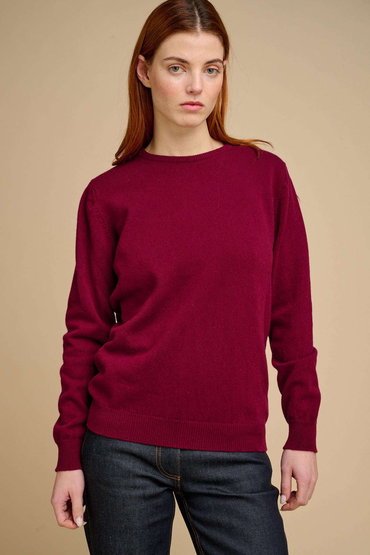 Woman wearing a burgundy sweater and dark jeans against a beige background