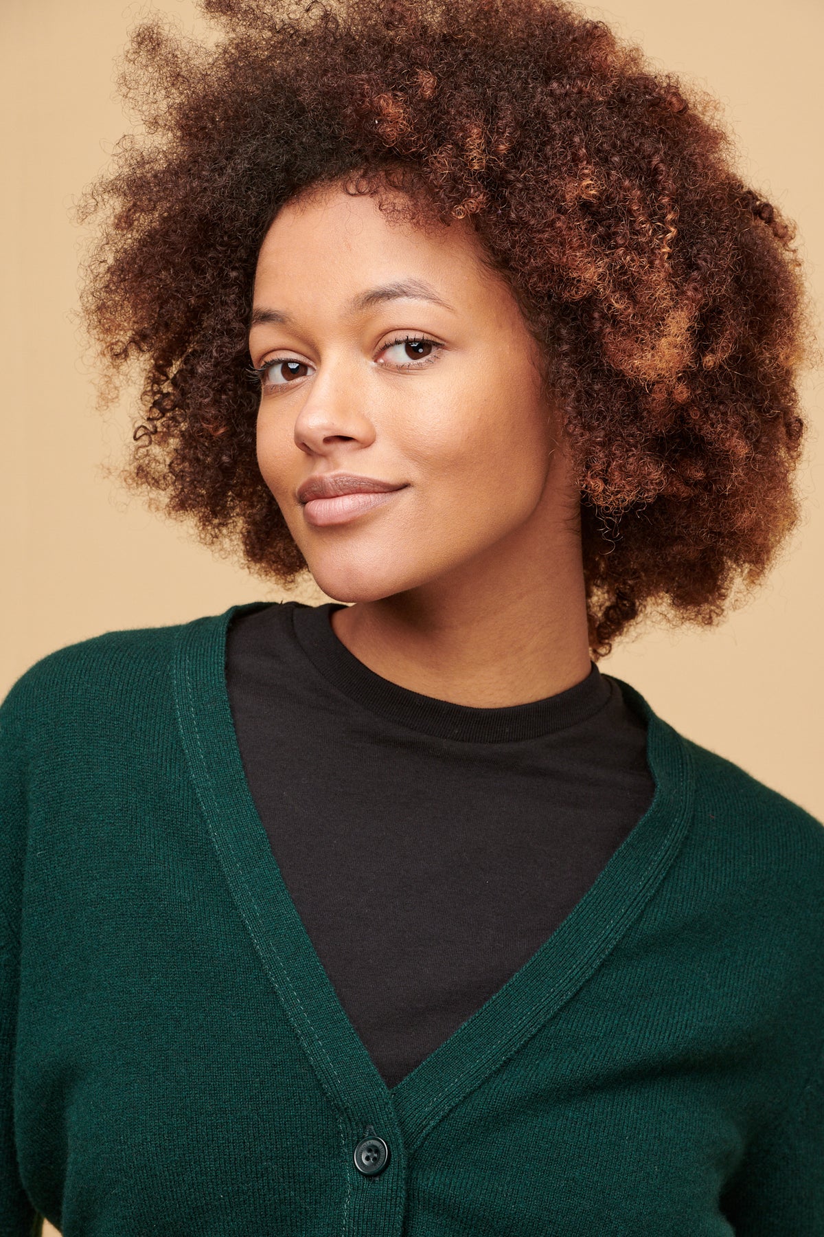 Portrait of femalewith curley brown hair wearing black t shirt with v neck cardigan in bottle green over the top