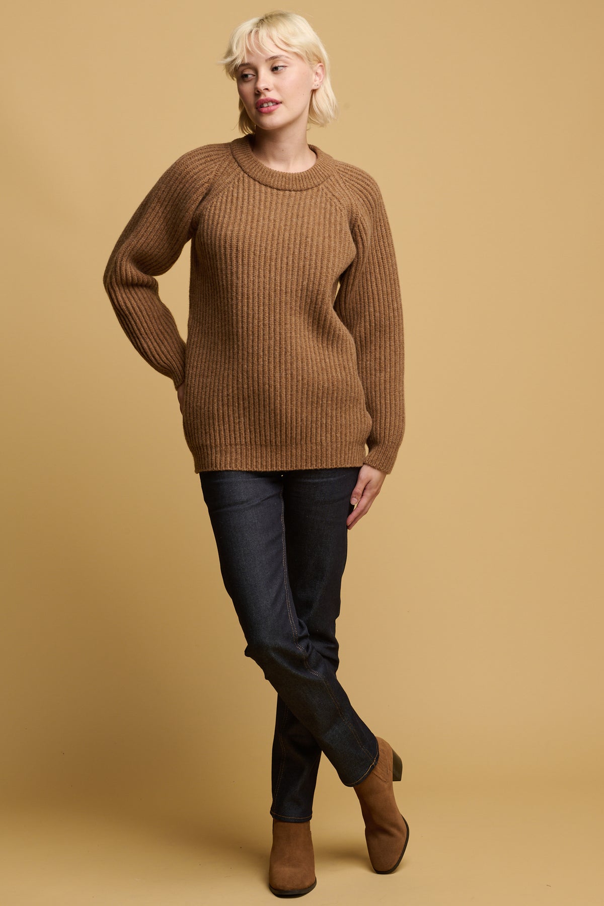 female wearing lambswool fisherman ribbed jumper in dark camel paired with straight leg jeans in indigo and dark camel coloured suede boots