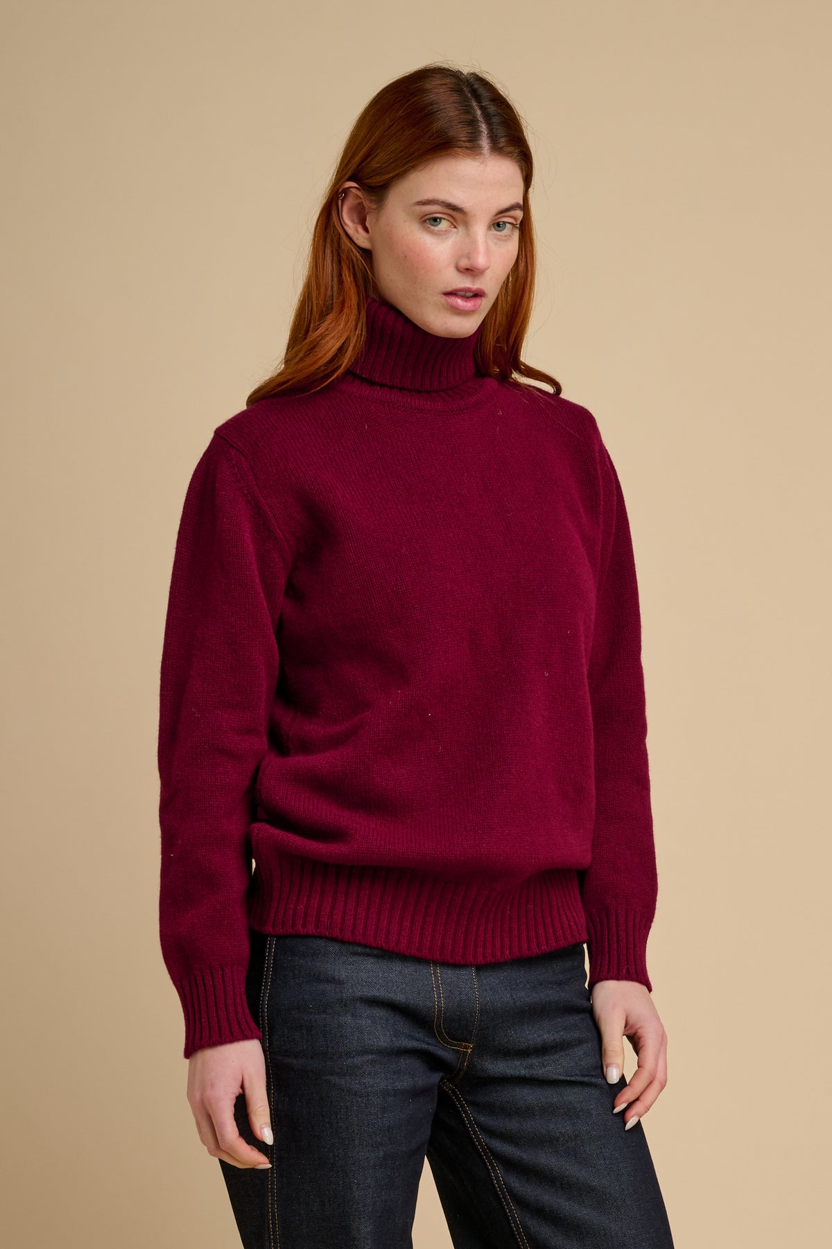 Woman wearing lambswool roll neck jumper in burgundy.