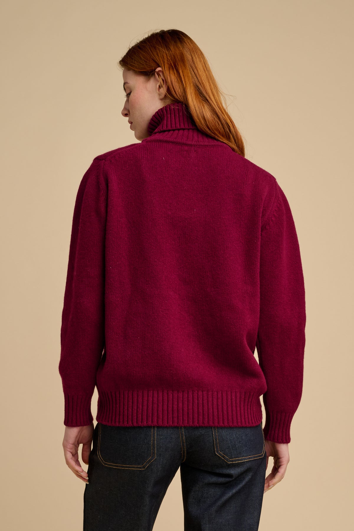 The back of woman wearing lambswool roll neck jumper in burgundy.