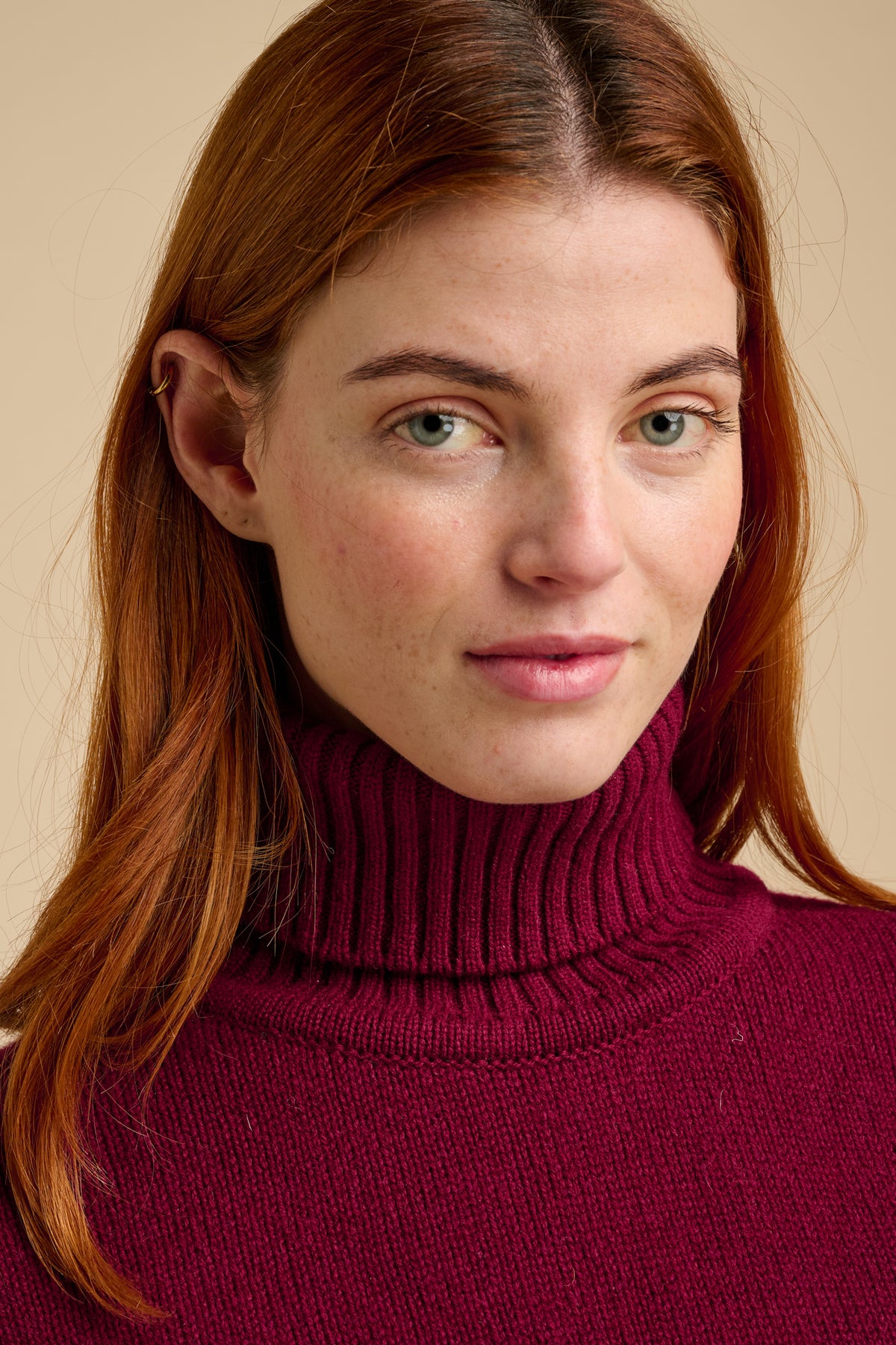 Woman wearing lambswool roll neck jumper in burgundy.