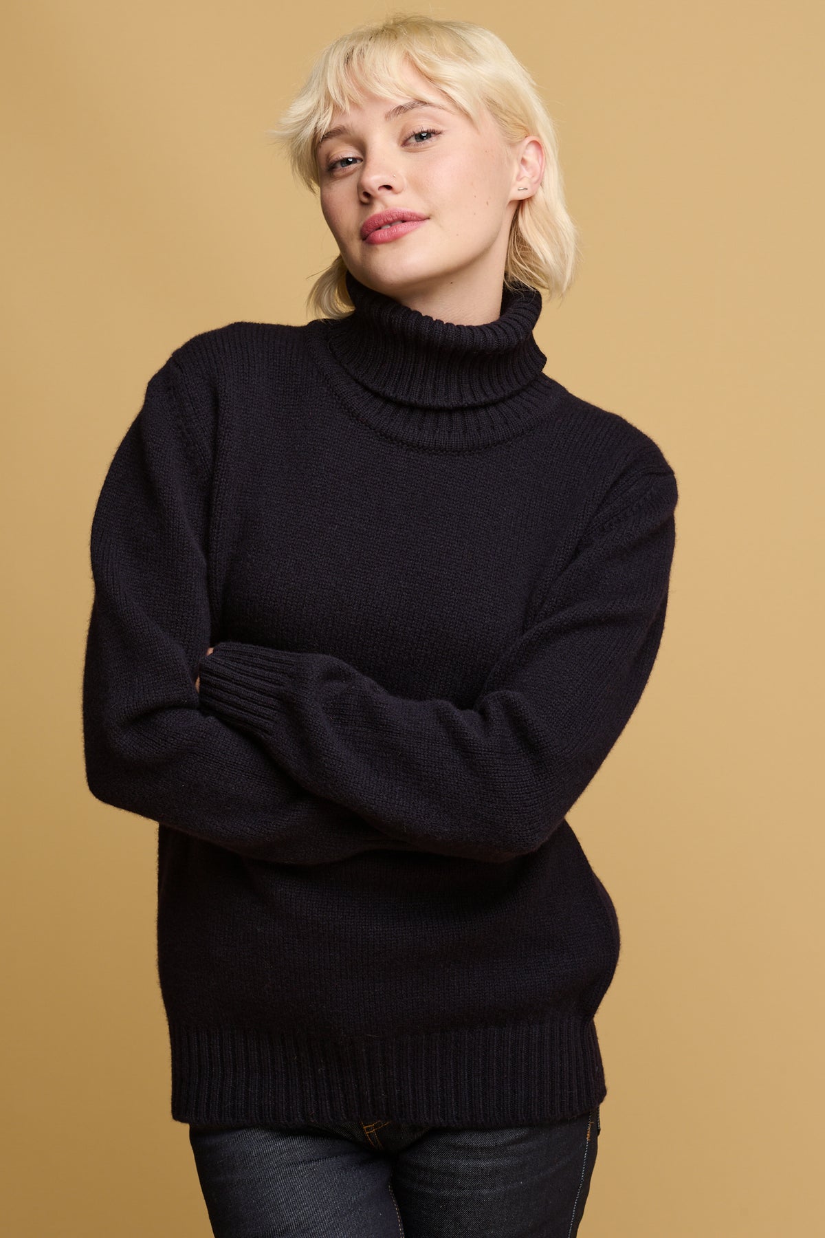 Thigh up image of female with her arms folded looking smug in her community clothing lambswool roll neck jumper in navy