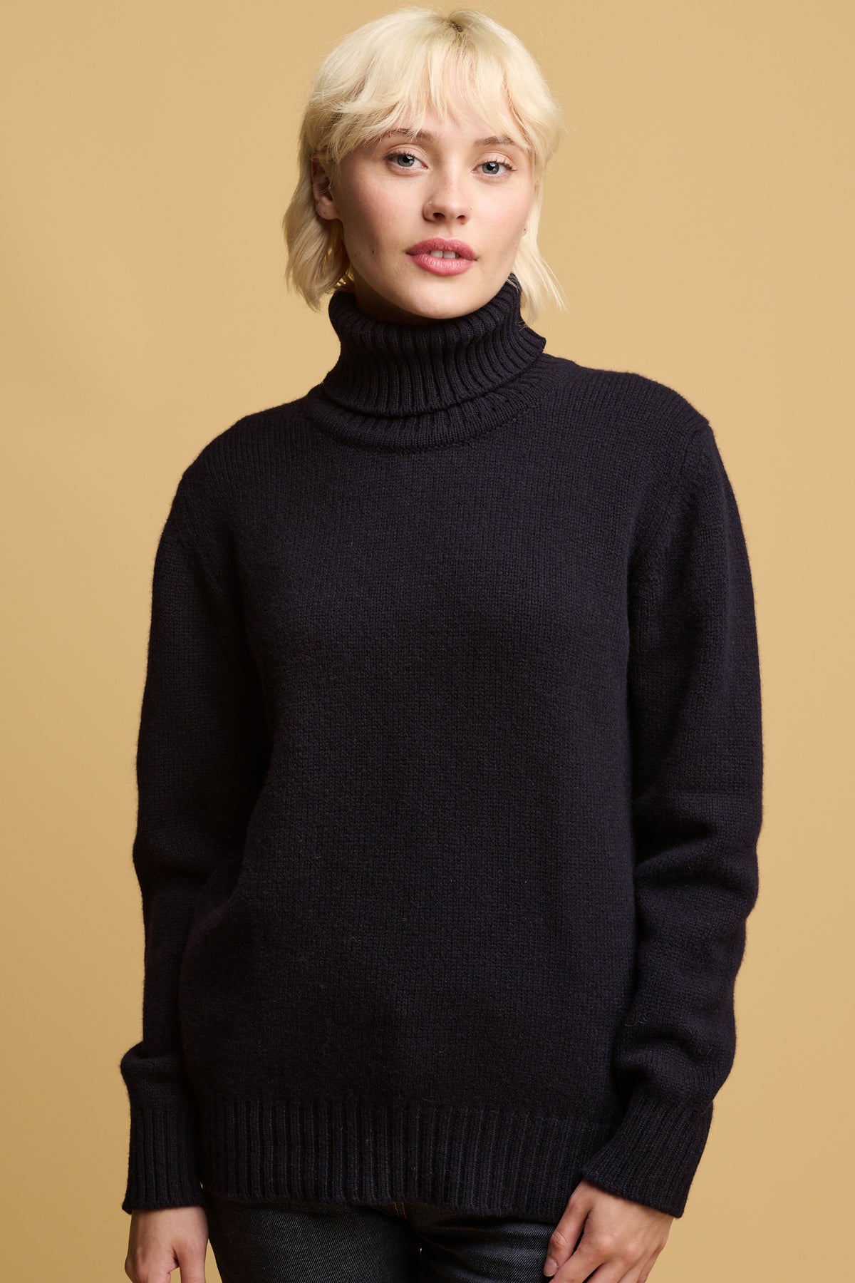 Thigh up image of female wearing community clothing lambswool roll neck jumper in navy