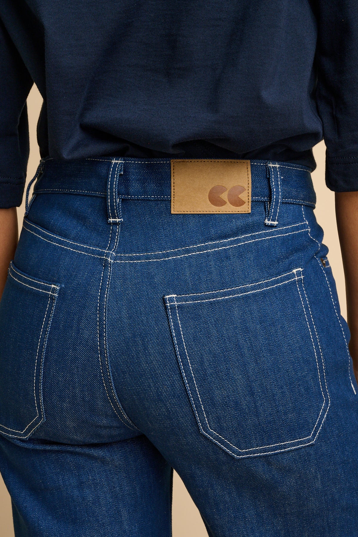 The back of woman wearing blue jeans with a visible brand logo on the waistband.