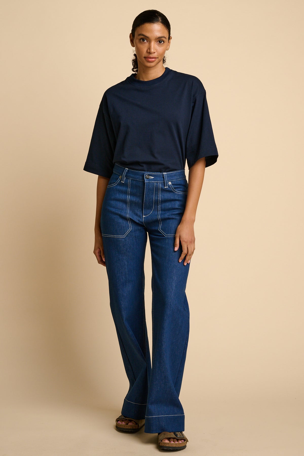 Woman wearing a navy t-shirt and blue jeans against a beige background