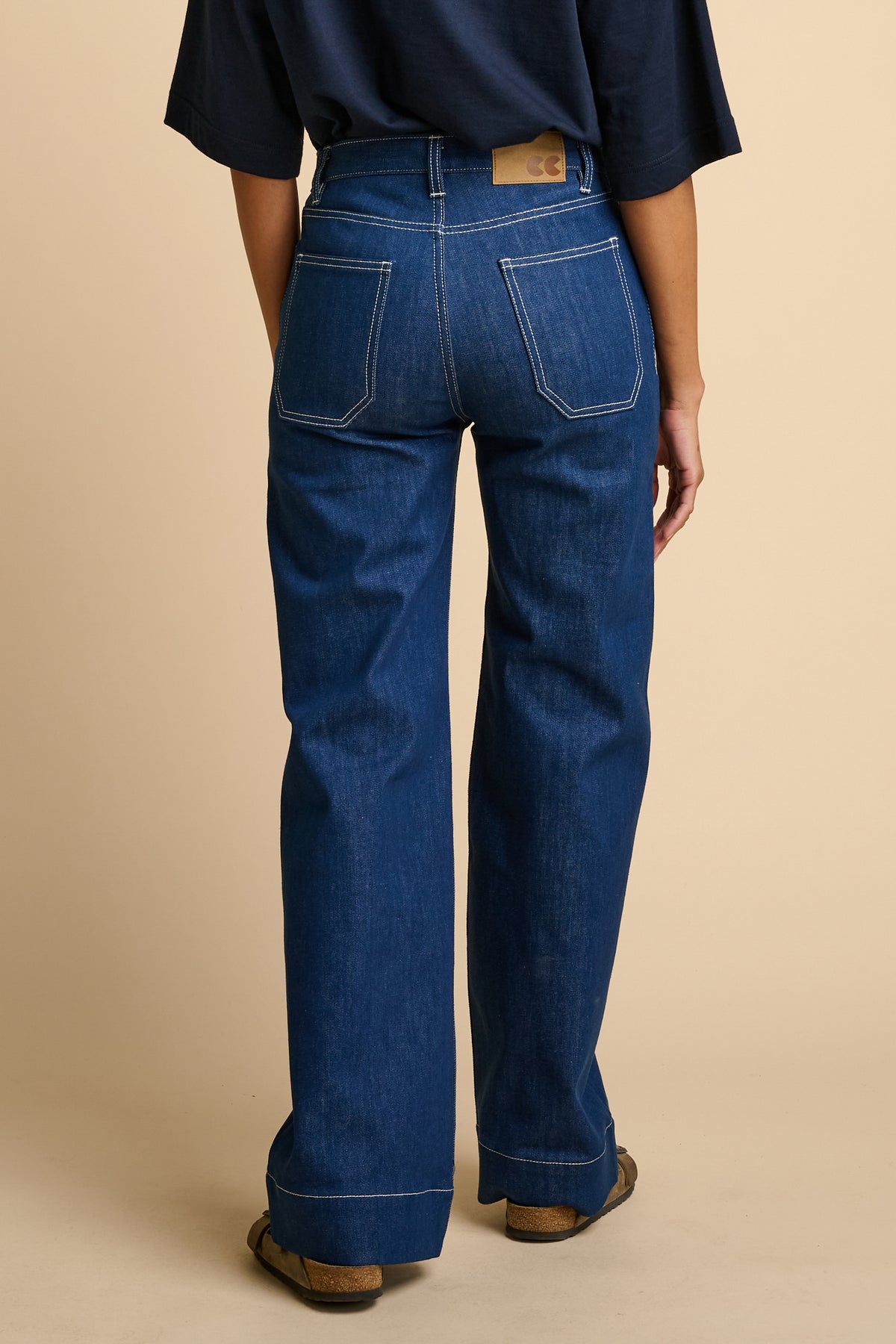 Woman wearing blue jeans on a beige background.