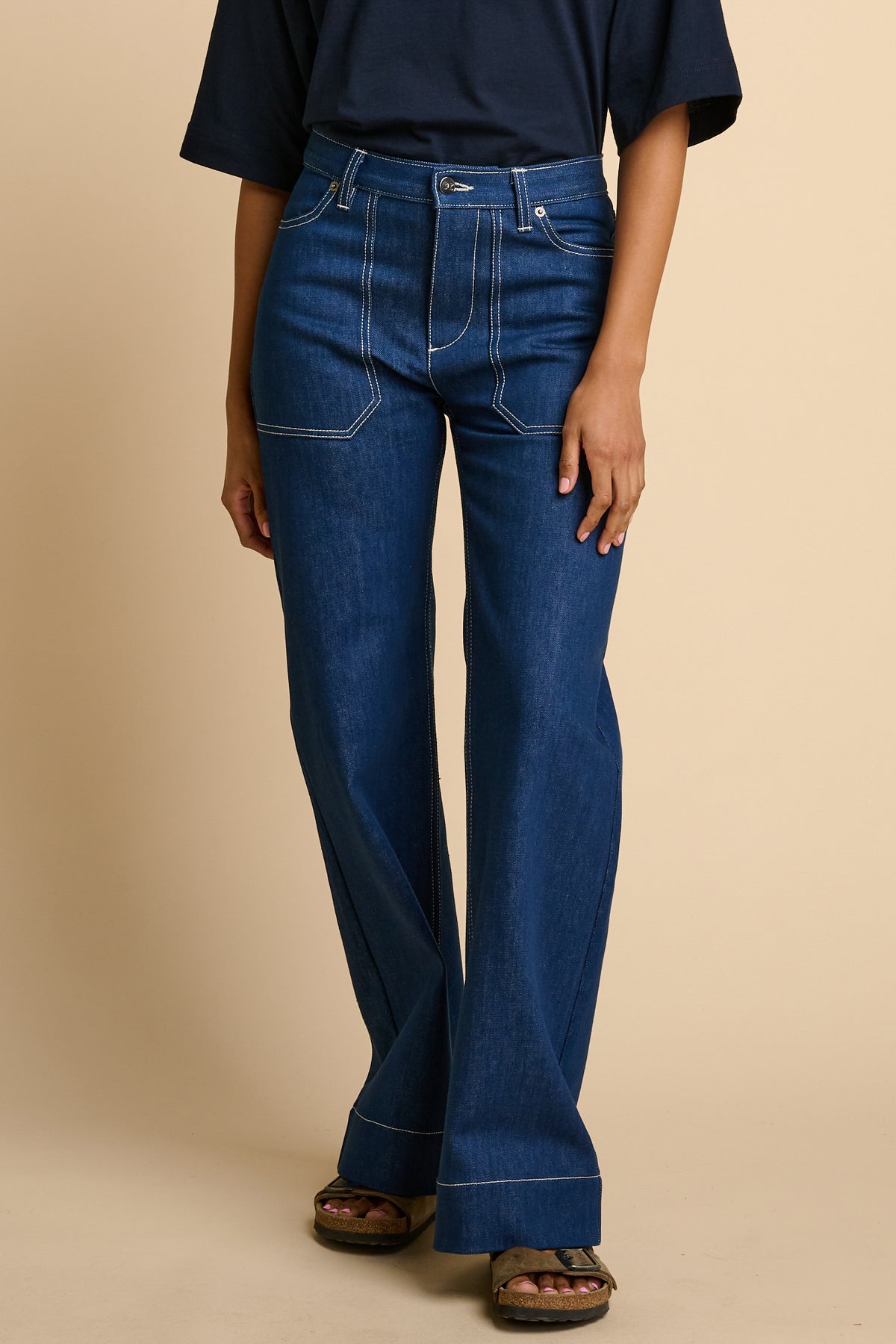 Woman wearing blue flared jeans on a beige background.
