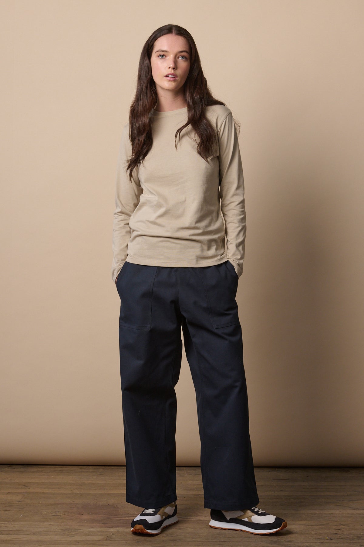 Full body image of brunette female wearing long sleeve t shirt in stone