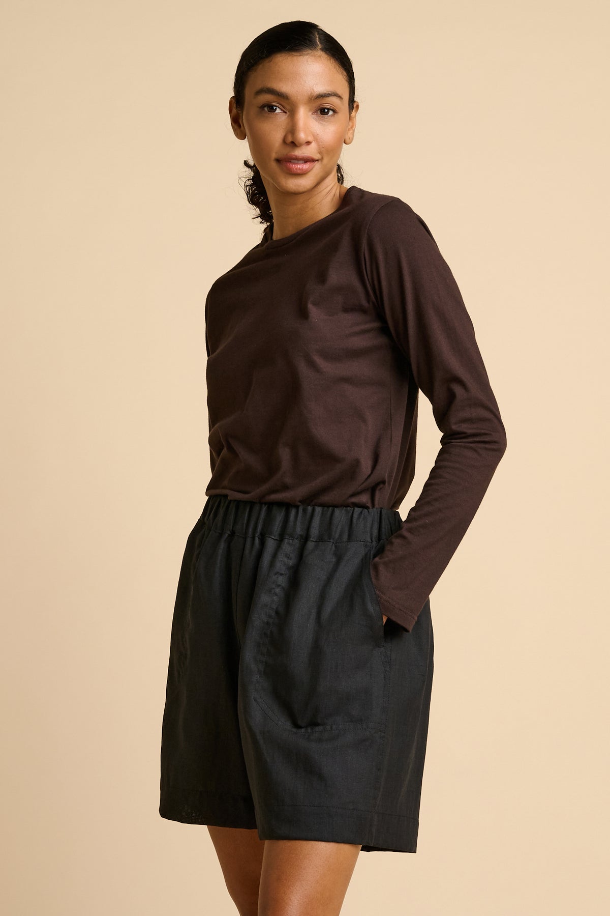 Woman wearing a brown long-sleeve top and black shorts on a beige background.