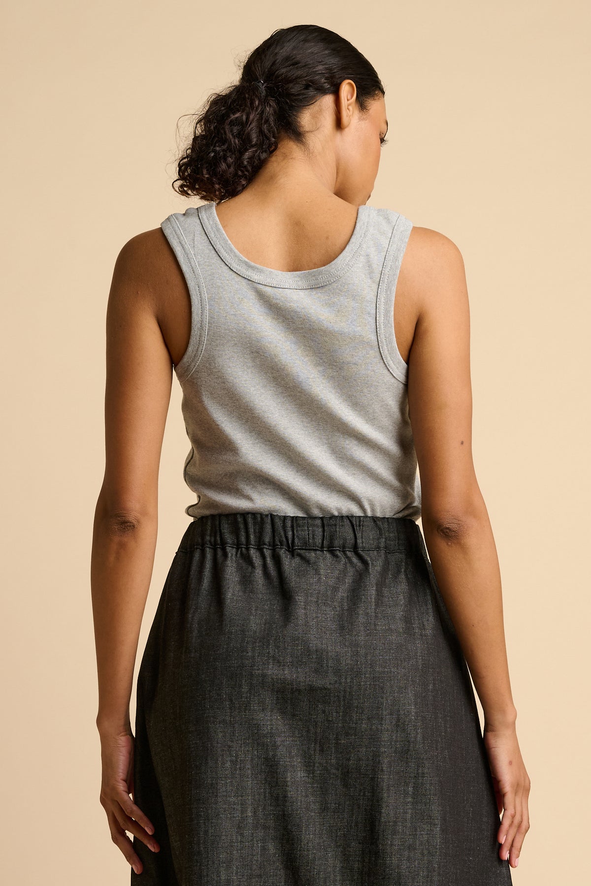 Woman wearing a grey tank top and black skirt on a beige background.