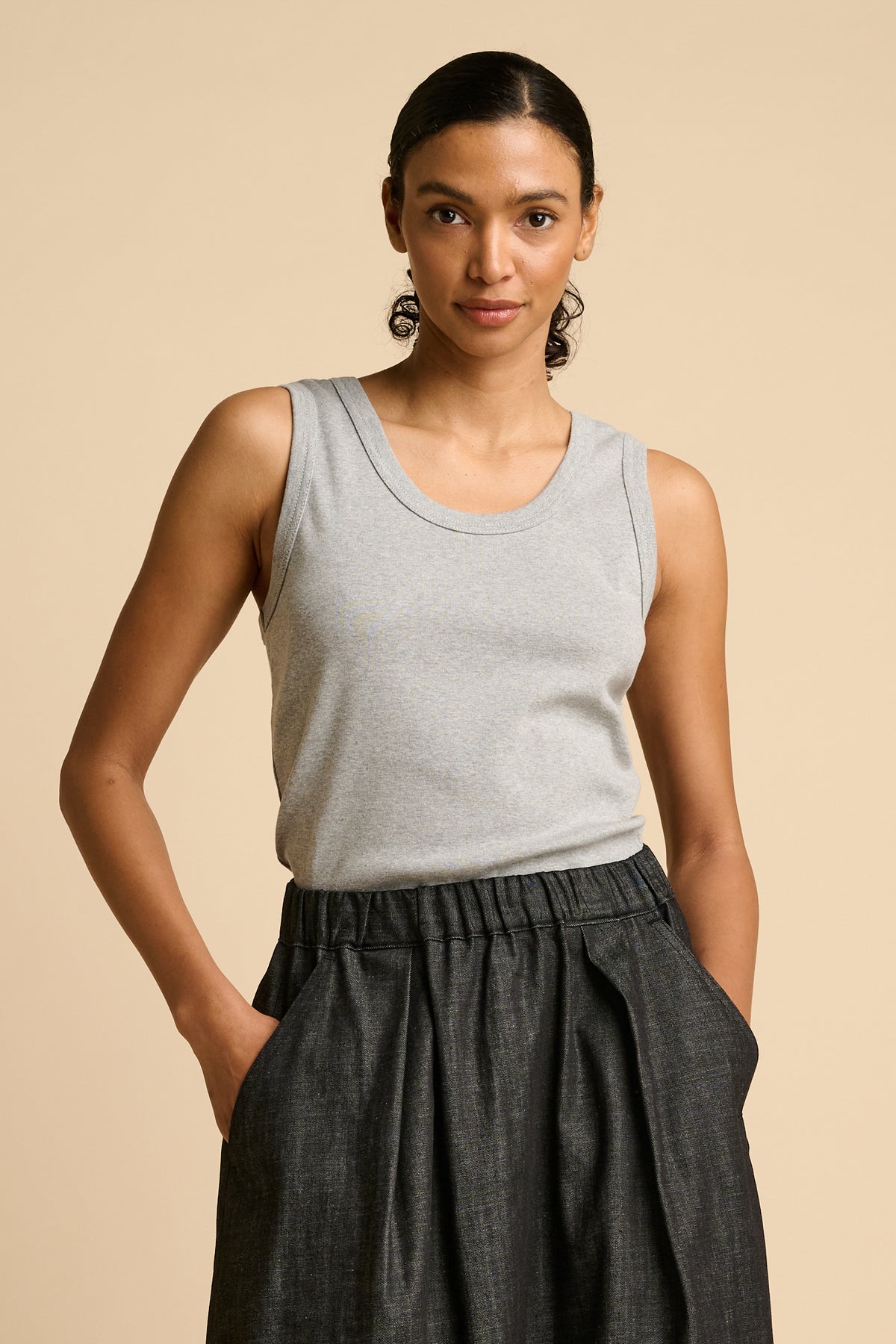 Woman wearing a grey tank top and black skirt on a beige background.