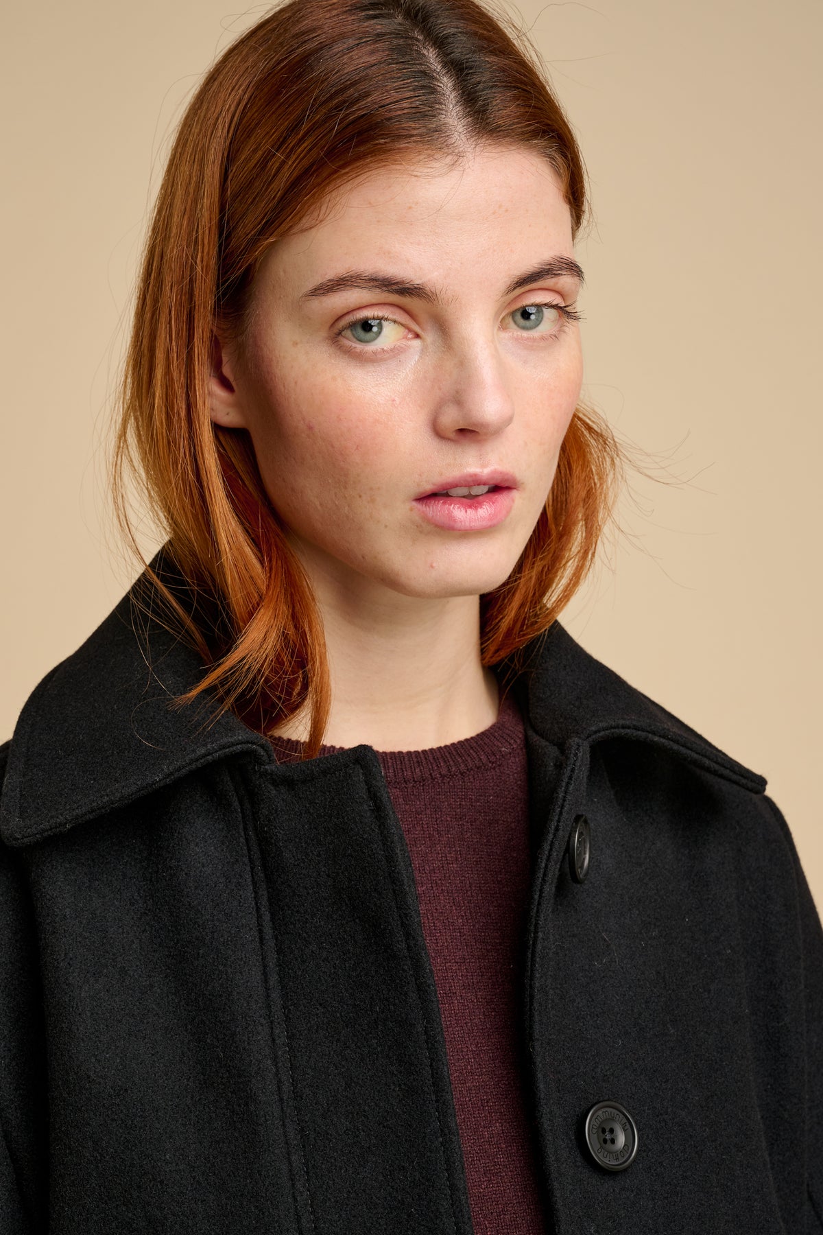 Woman wearing wool jacket in black against beige background..