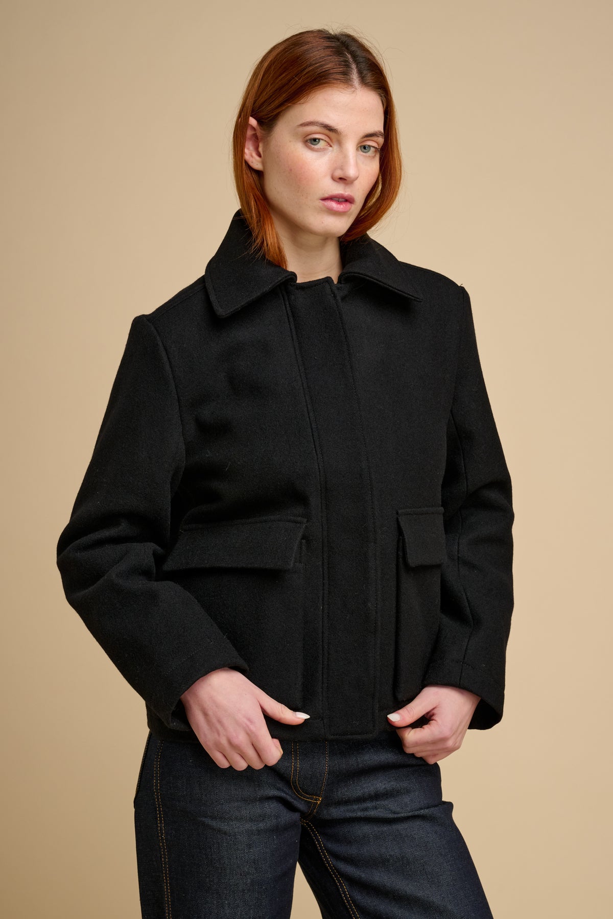 Woman wearing a black wool coat against a beige background