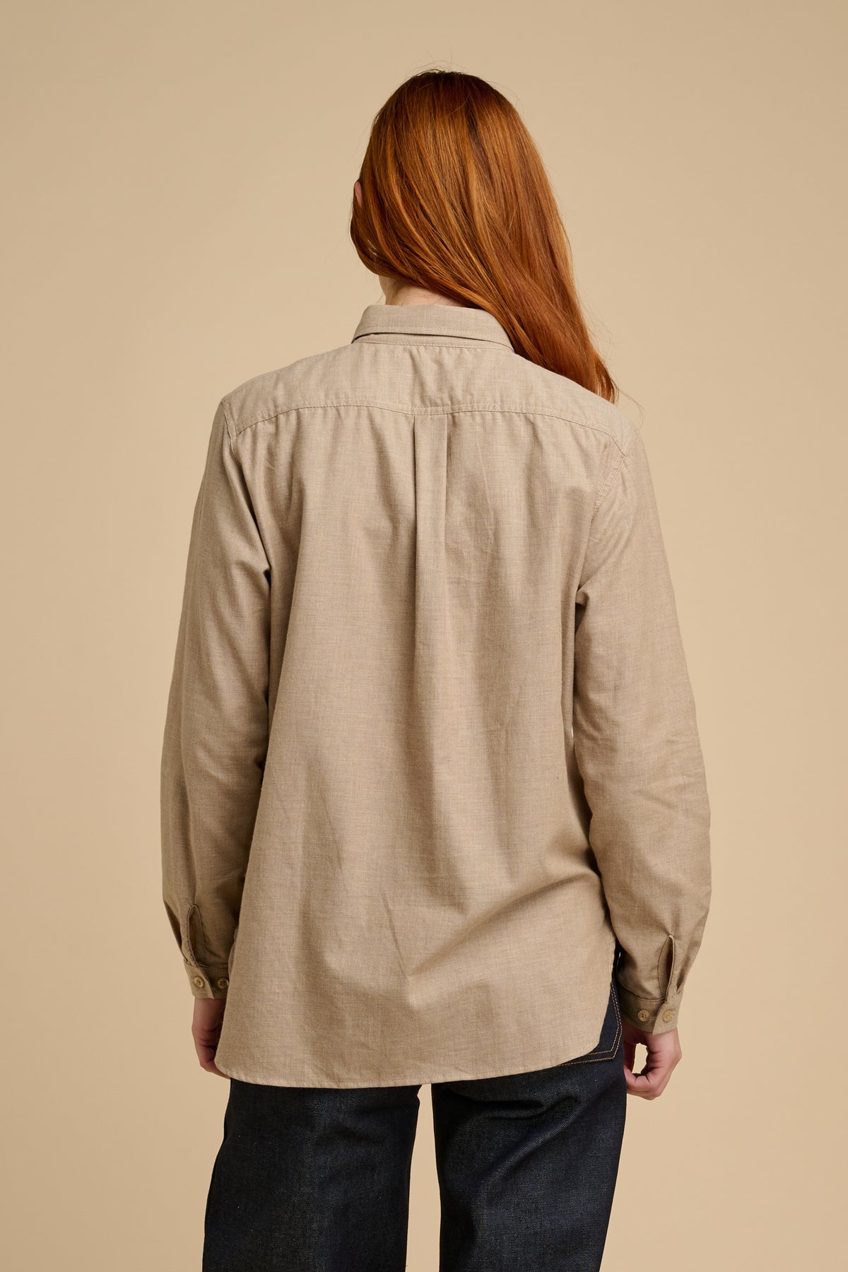 The back of woman wearing beige shirt against a beige background