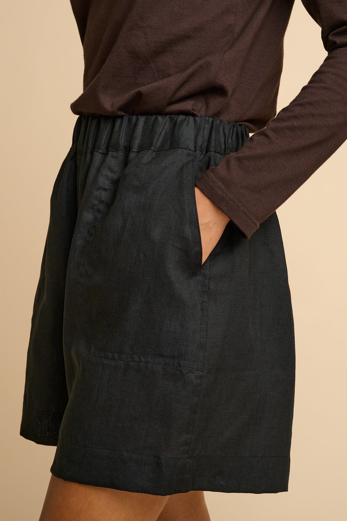 Black shorts worn with a brown long-sleeve top on a beige background