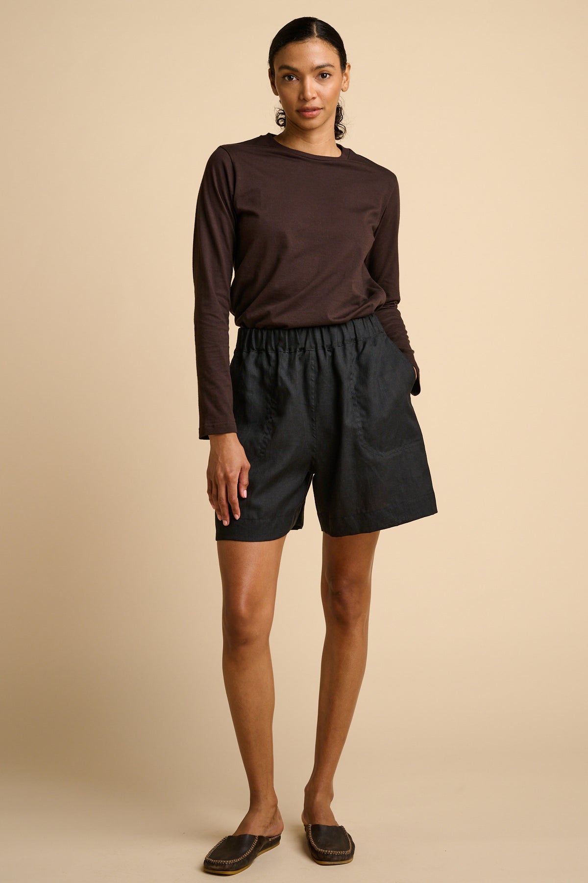 Woman wearing a brown long-sleeve top and black shorts on a beige background.