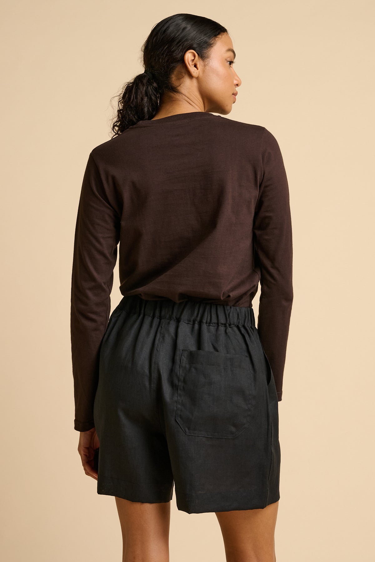 Woman wearing a brown long-sleeve top and black shorts on a beige background.