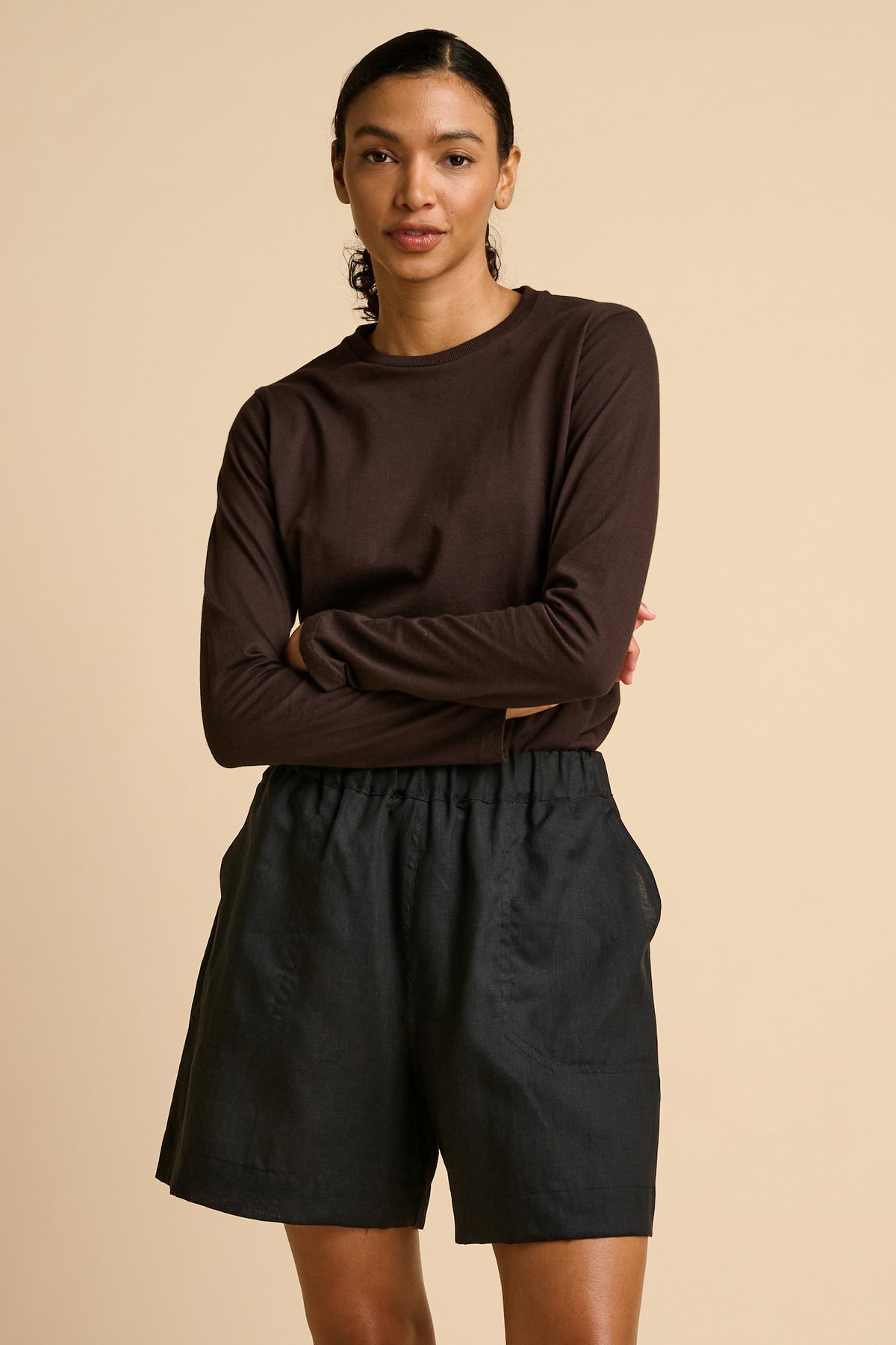 Woman wearing a brown long-sleeve top and black shorts on a beige background.