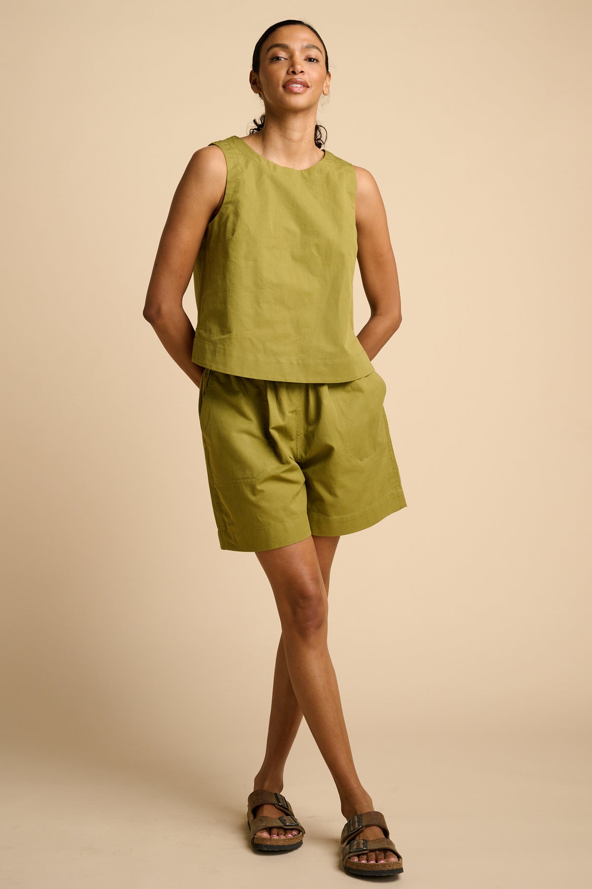Woman wearing a green sleeveless top and shorts on a beige background
