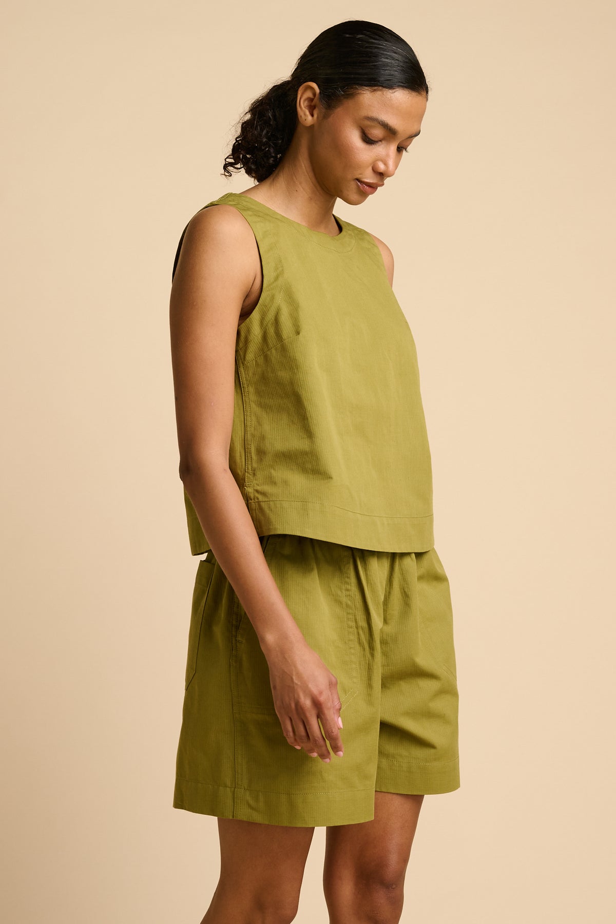 Woman wearing a green sleeveless top and shorts set on a beige background.
