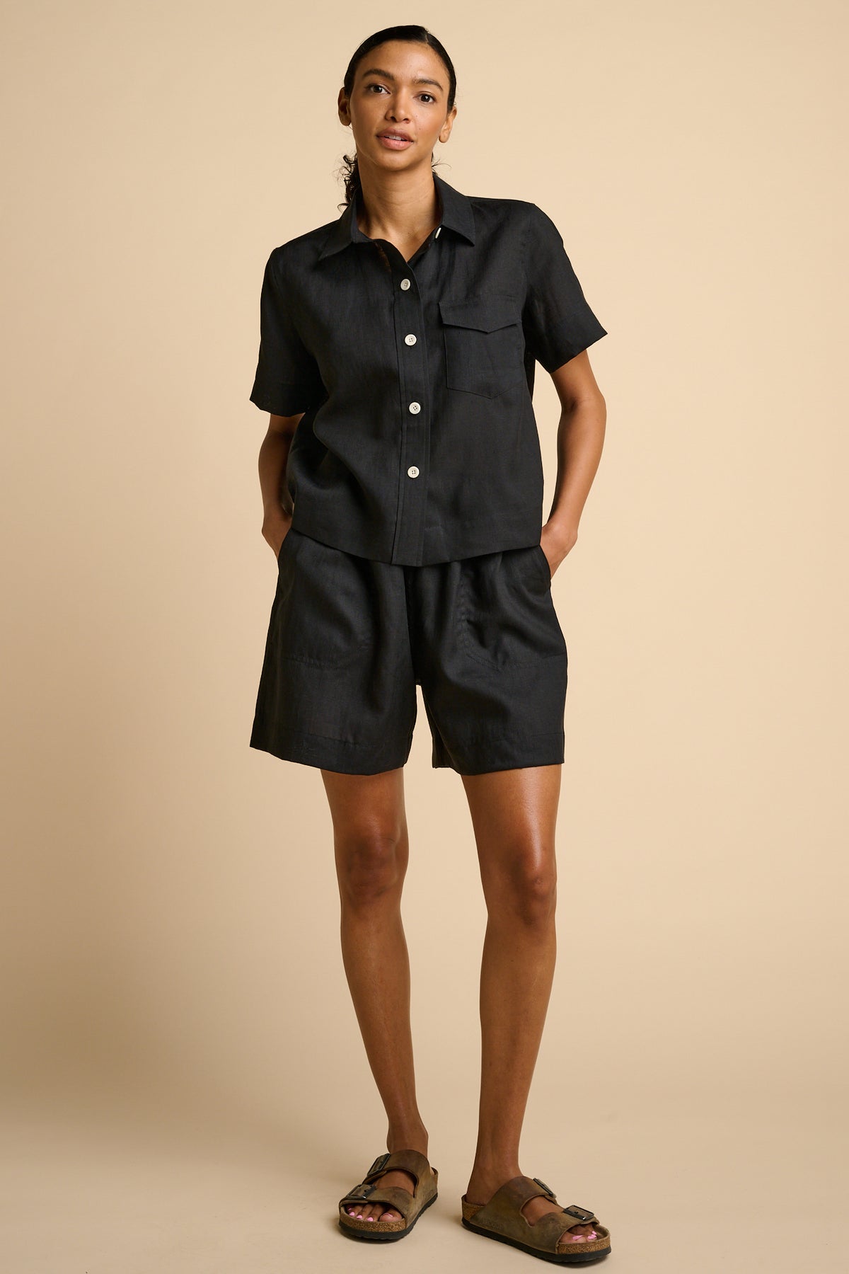 Woman wearing a black shirt and shorts set on a beige background.