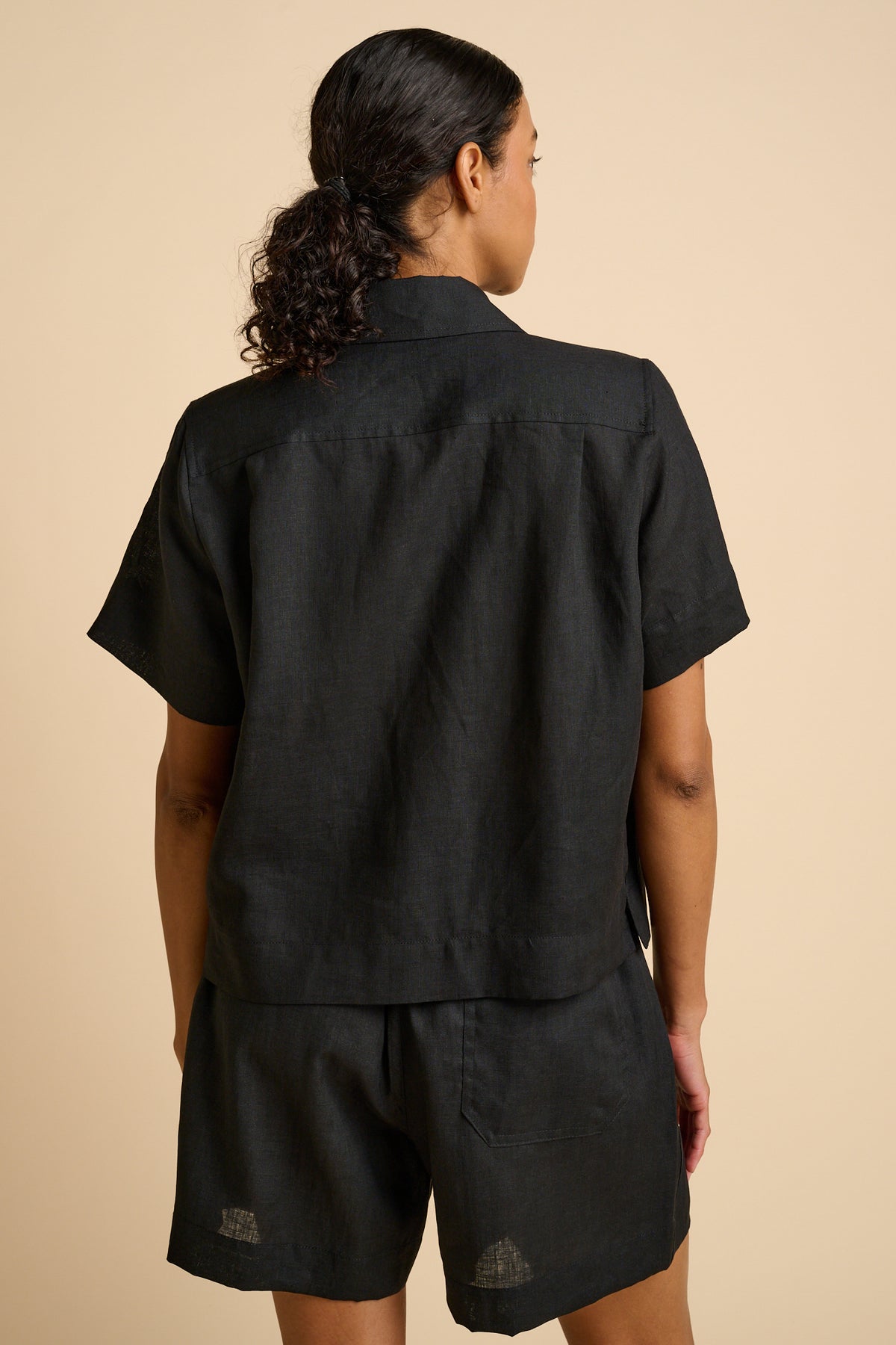 Woman wearing a black shirt and shorts set on a beige background.