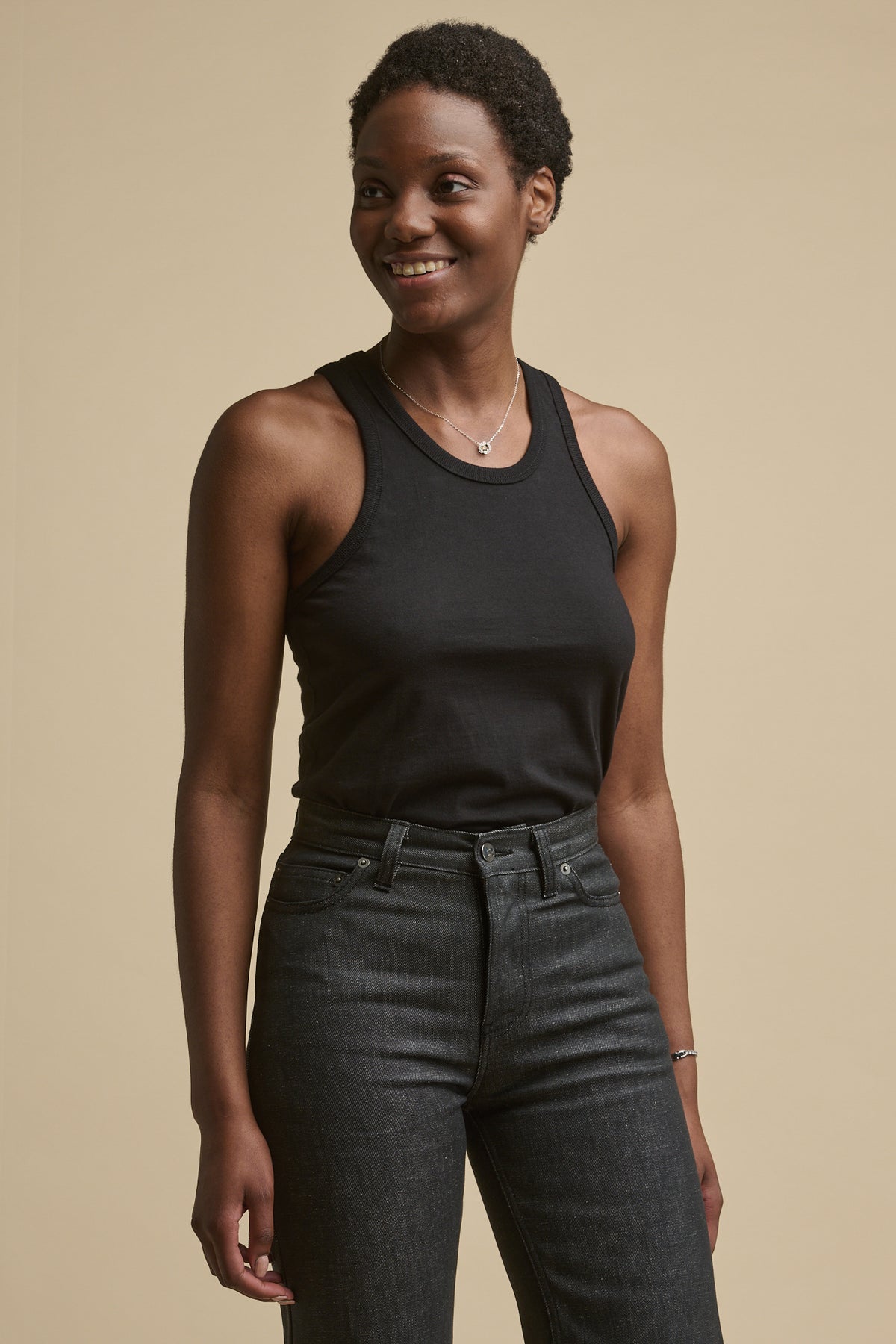 Thigh up image of the front of female wearing racer back vest in black tucked into high rise jeans in black