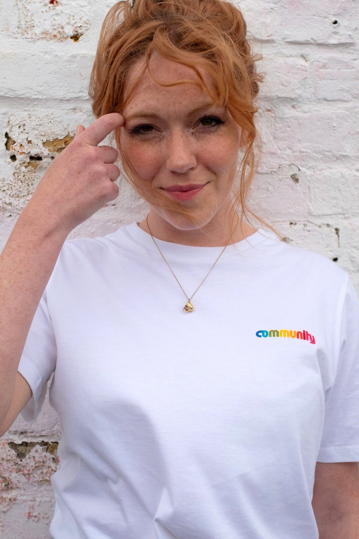 Actress Charlotte Spencer wearing a Short Sleeve white T-Shirt with branding on the chest, stood against a white brick wall