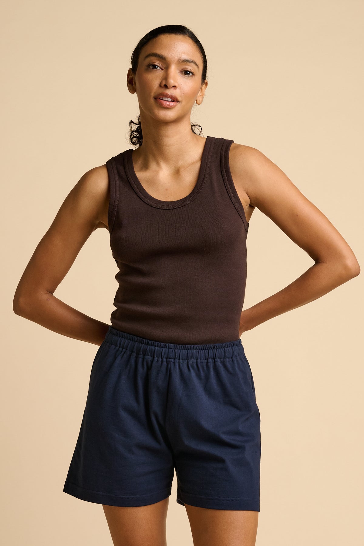 Woman wearing a brown tank top and navy shorts on a beige background