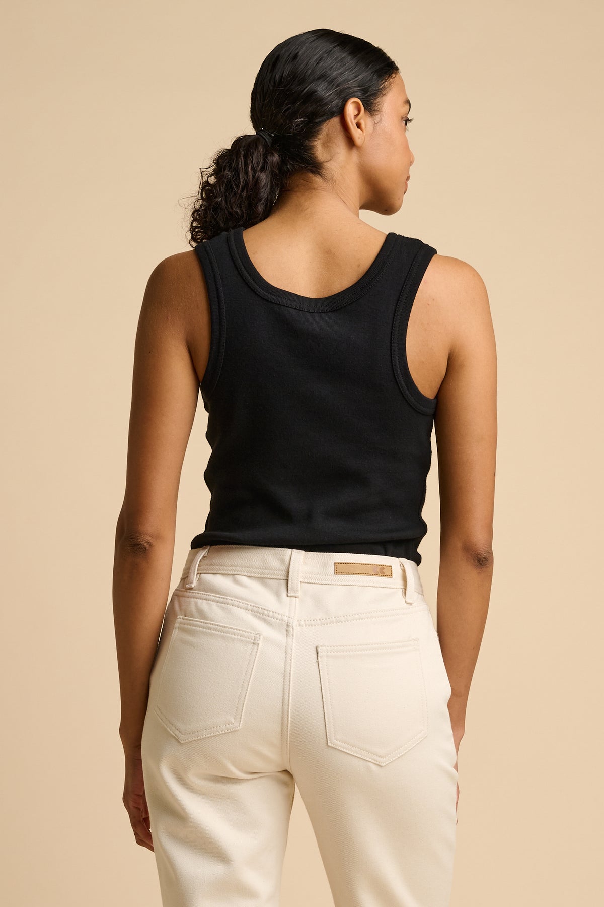 Woman wearing a black tank top and beige pants on a beige background