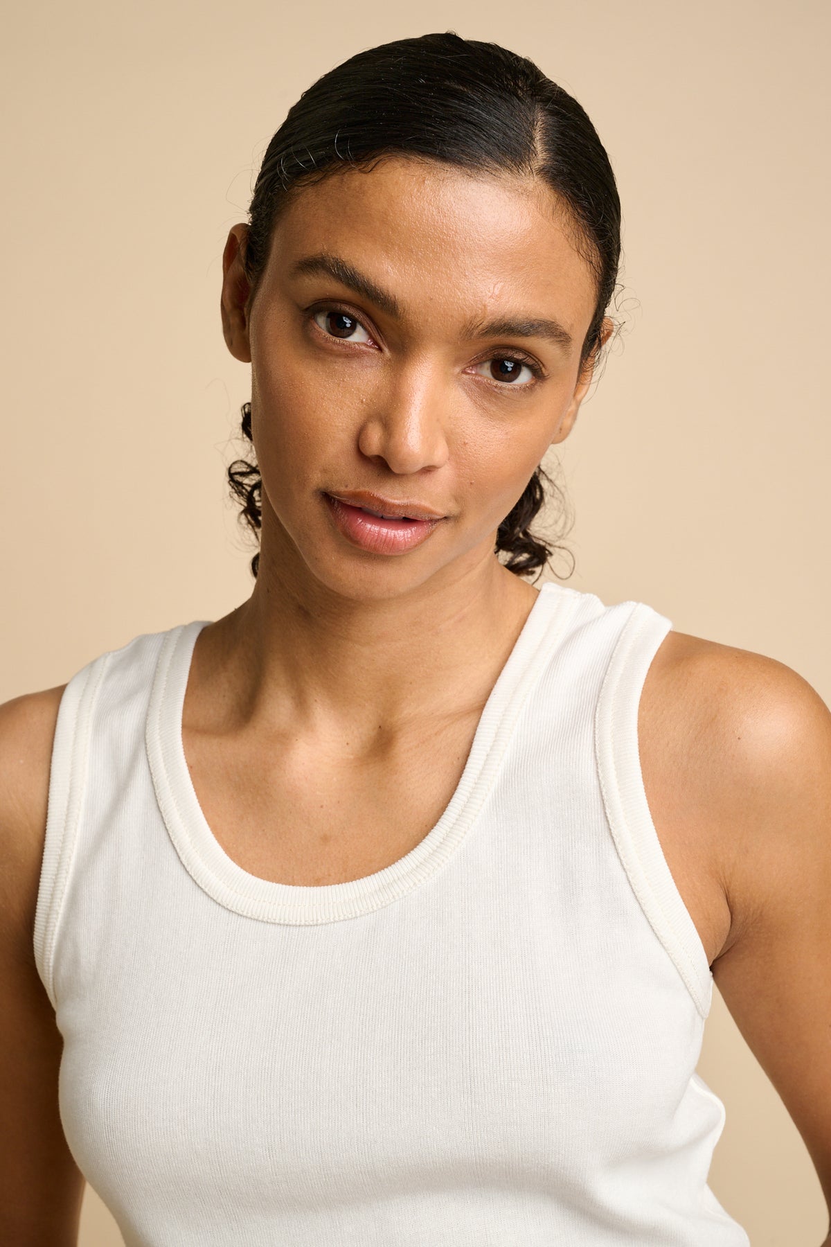Woman wearing a white tank top against a beige background