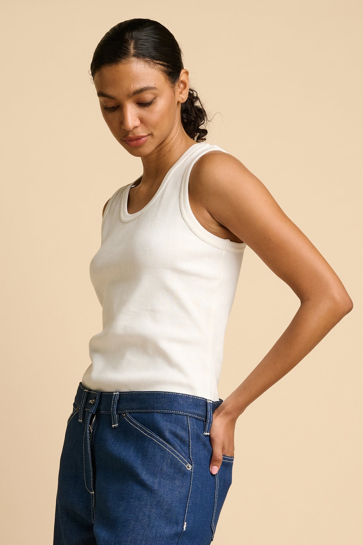 Woman wearing a white tank top and blue jeans on a beige background