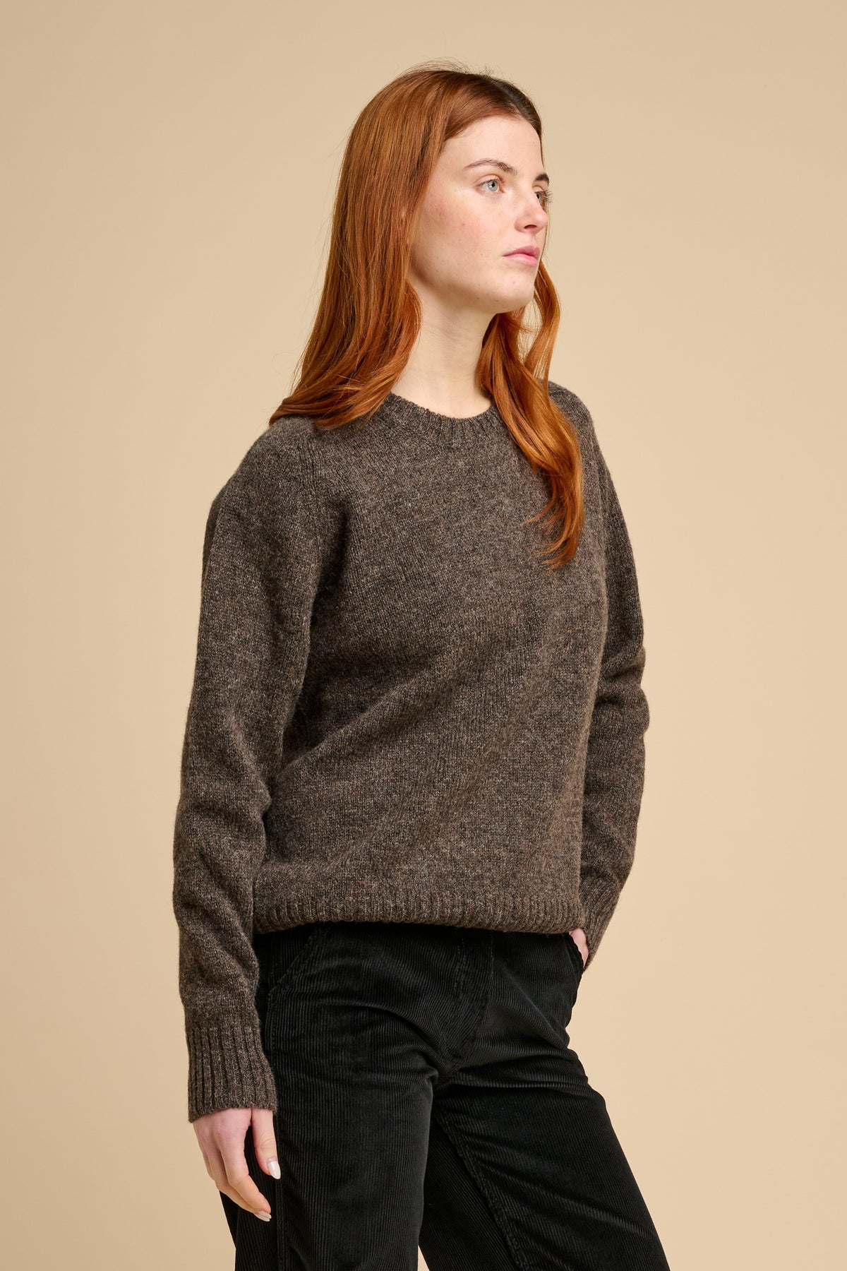 Woman wearing a brown knit jumper against a beige background.