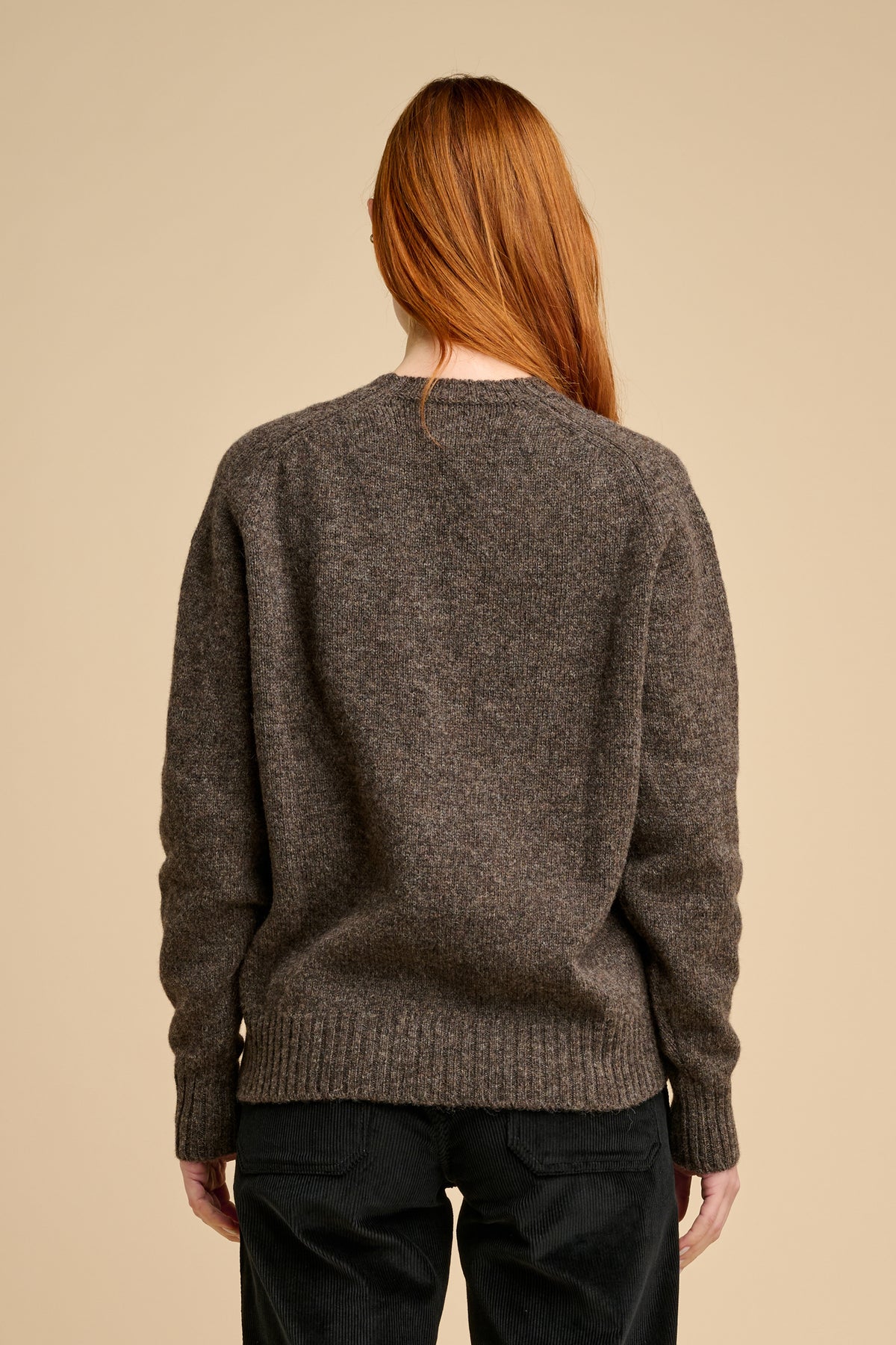 The back of woman wearing brown knit jumper against beige background