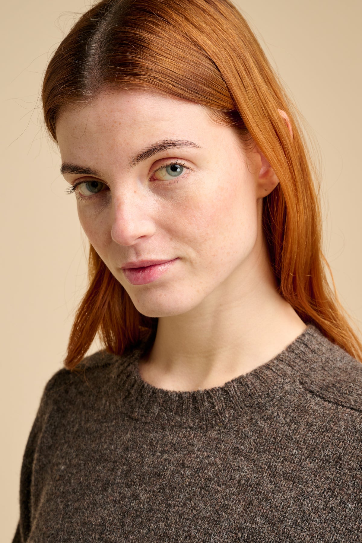 Woman wearing brown knit jumper against beige background.