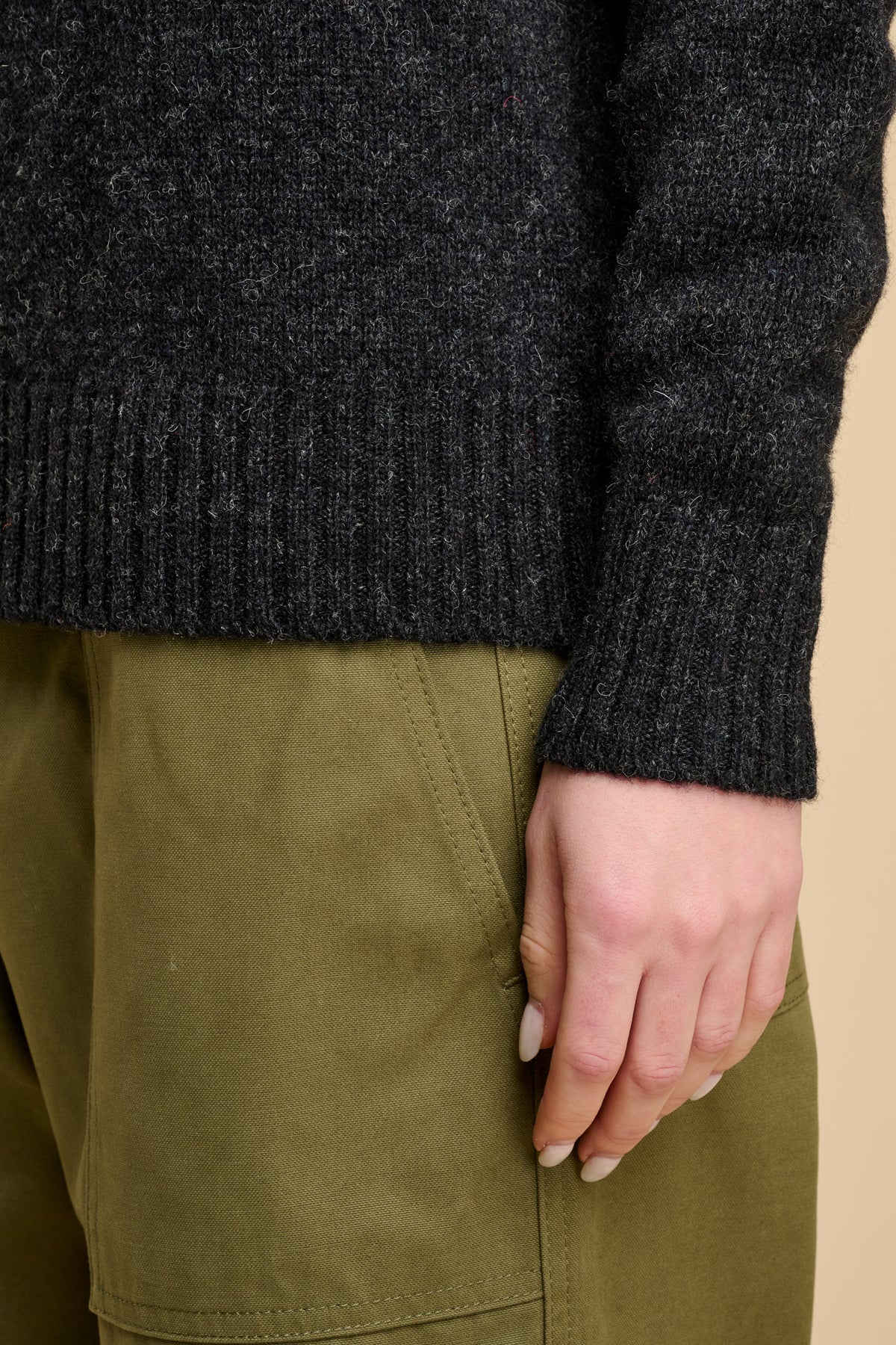 Woman wearing a charcoal marl knit jumper and green pants on a beige background